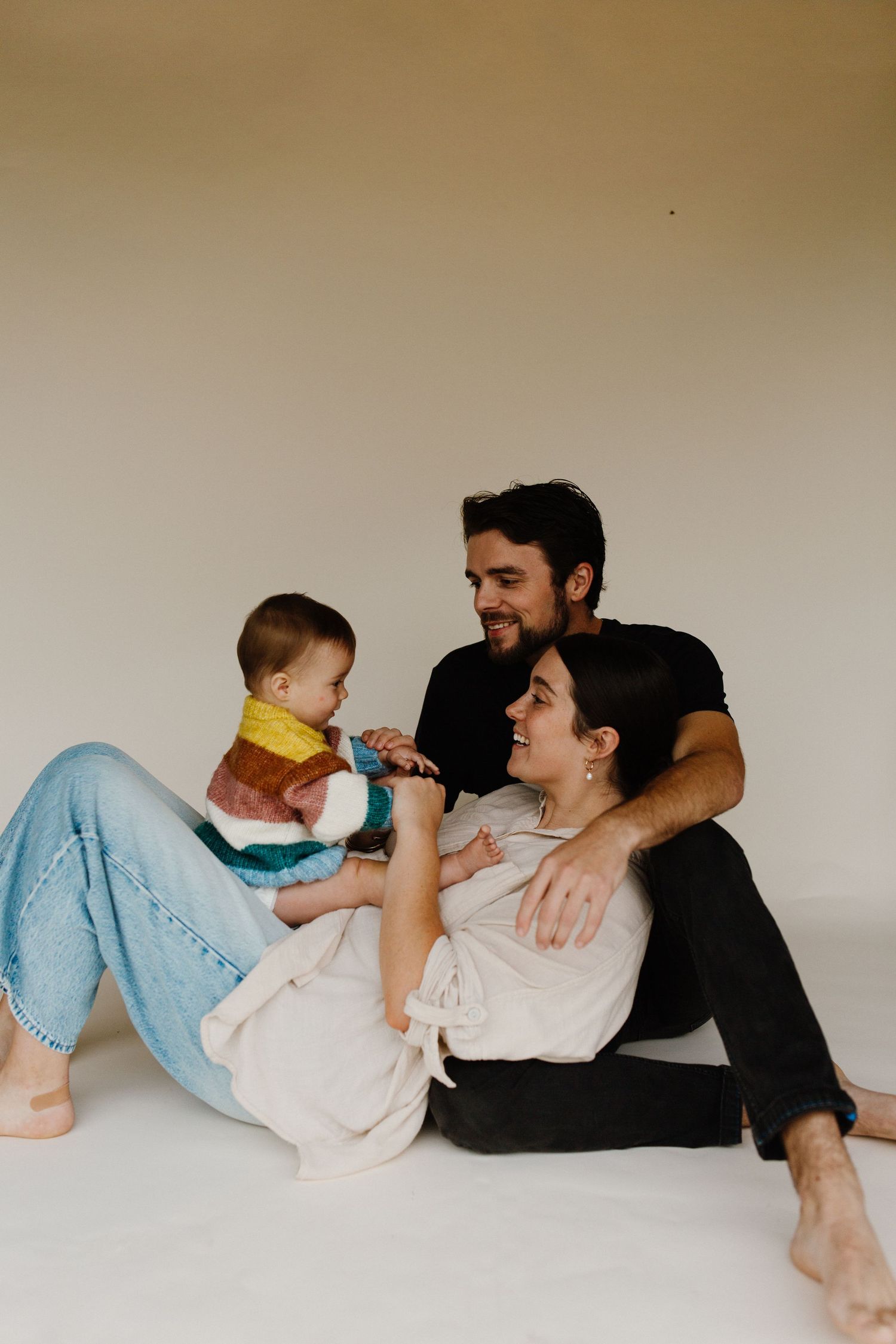 Family lying together on floor sharing playful moments in casual attire.