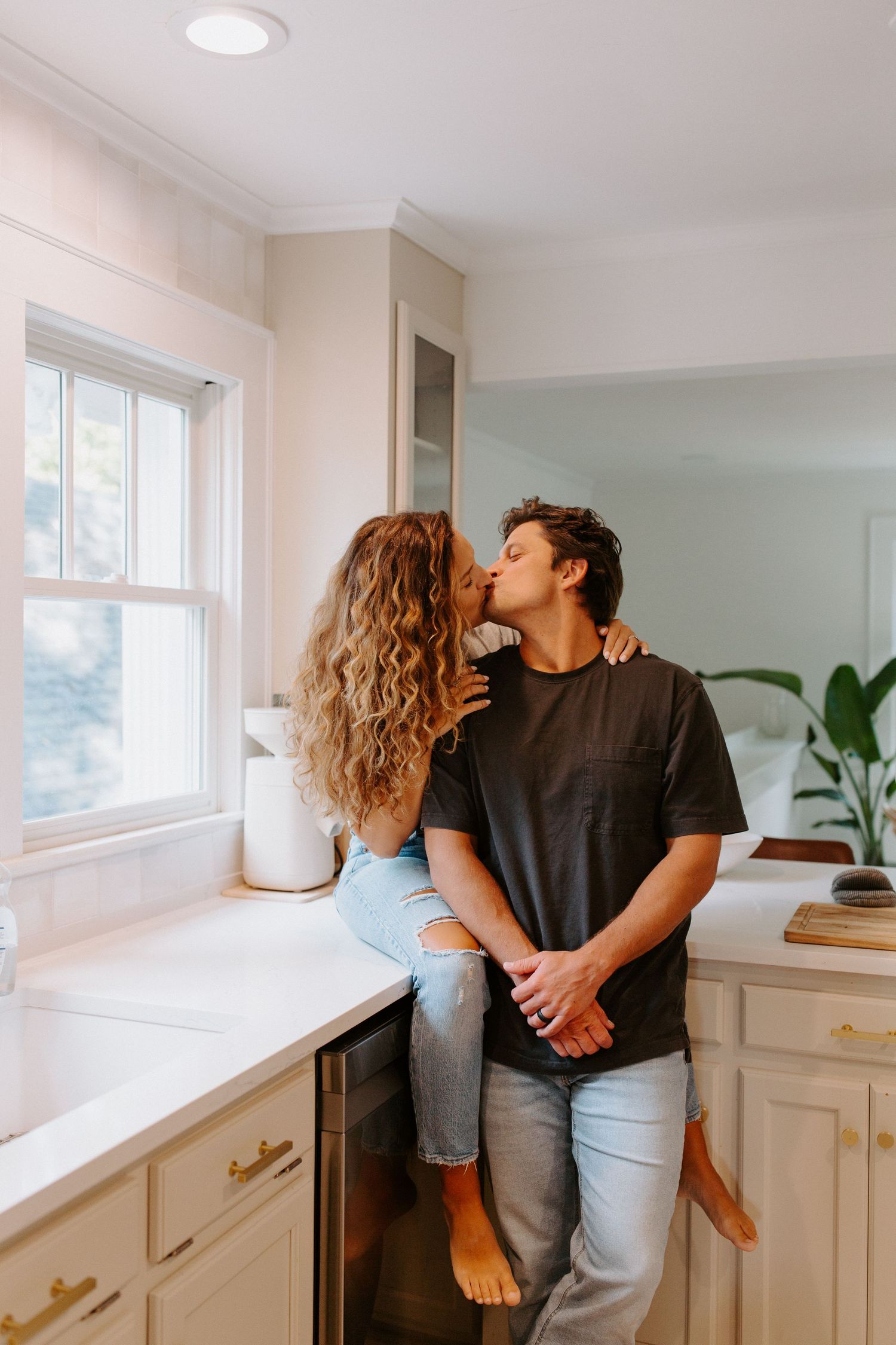 Couple sharing romantic moments against white kitchen cabinets in natural light.