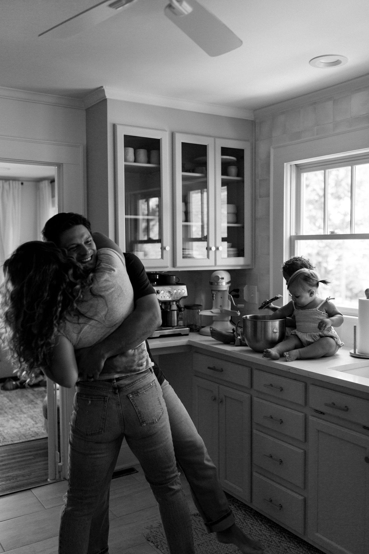 Candid black and white shots of family members embracing in a modern kitchen setting.