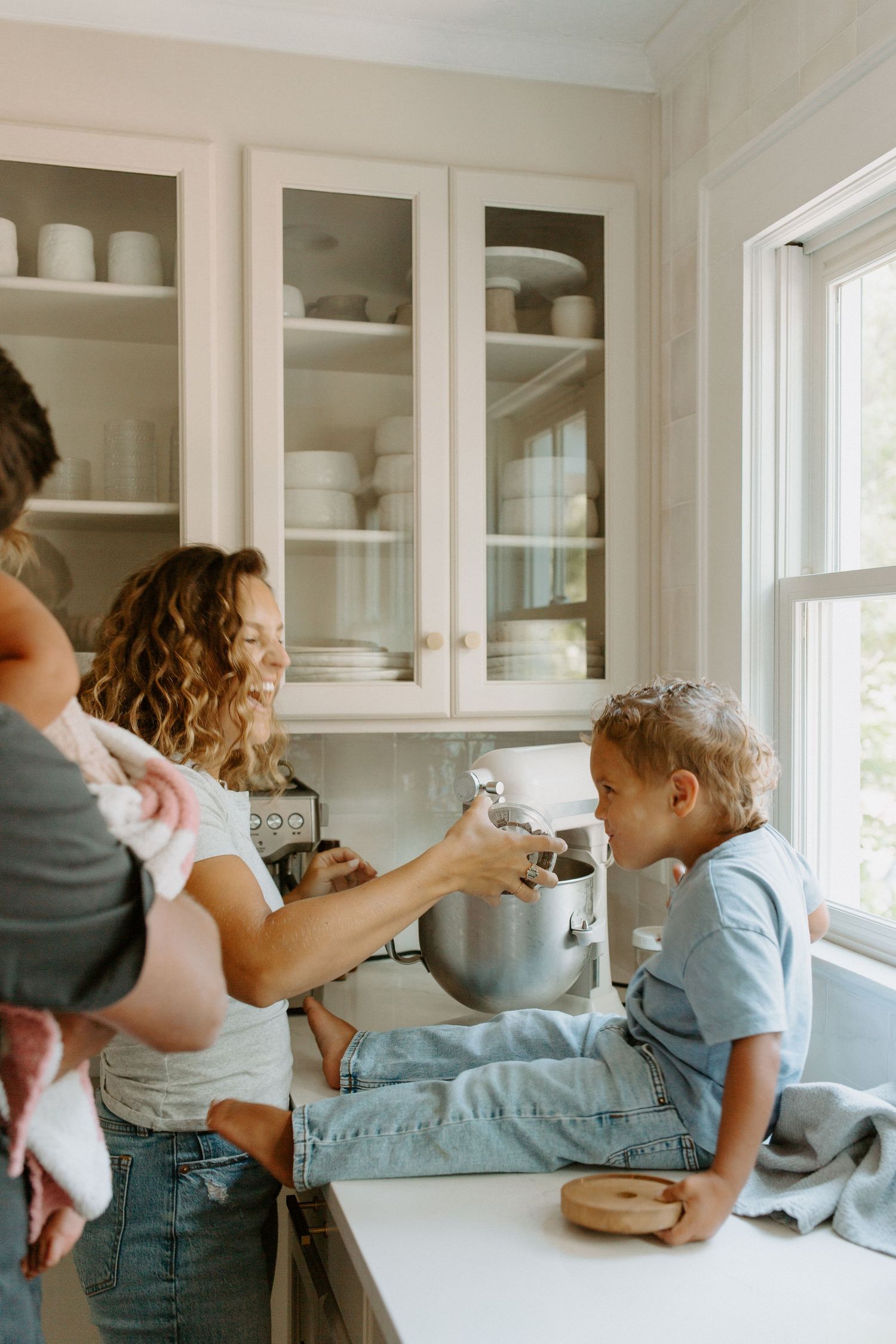 Family gathering in bright white kitchen with glass cabinets while baking together.