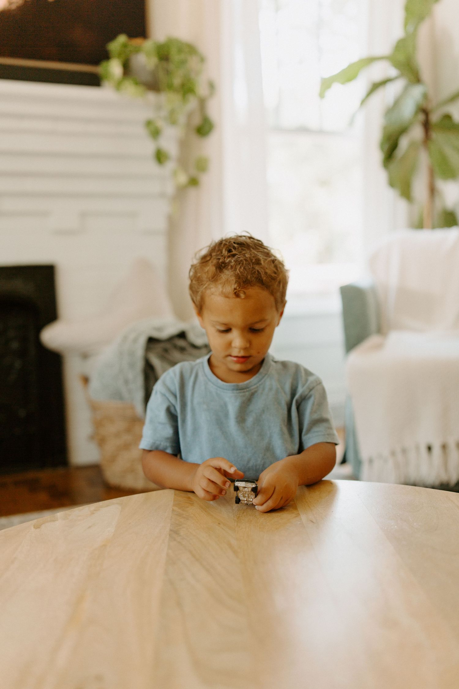 A child sits at a wooden table in a bright sunlit room.