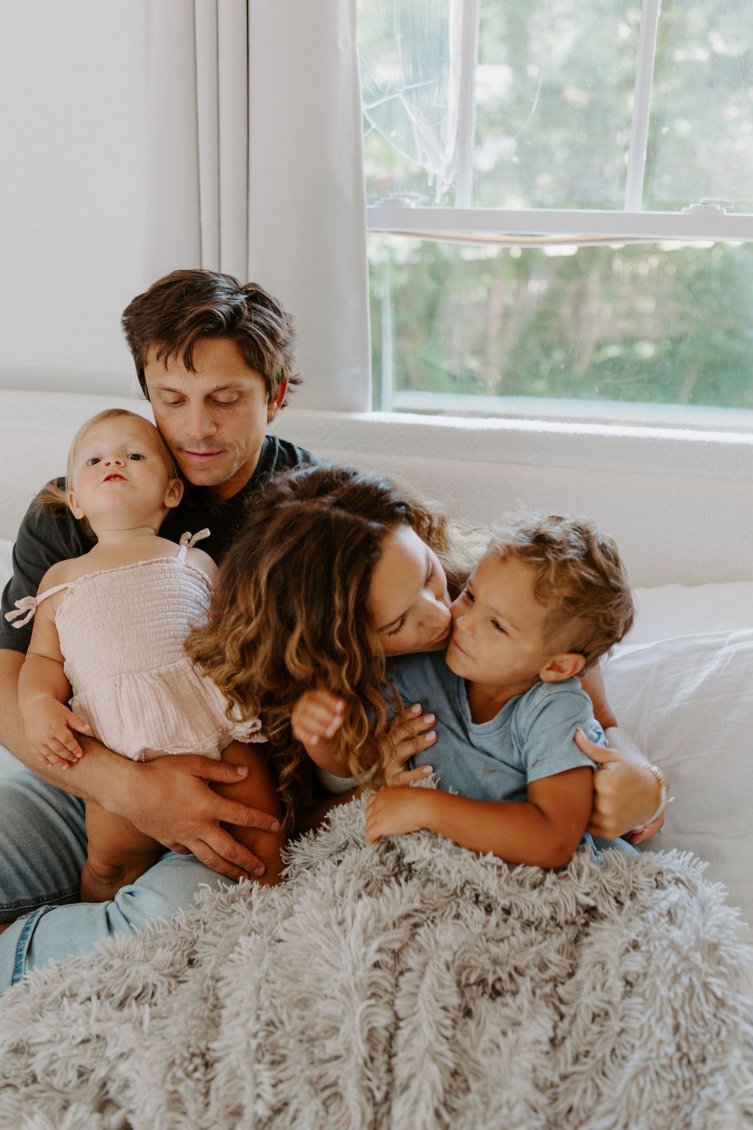 A family shares loving embraces while lying together on a fluffy white blanket.