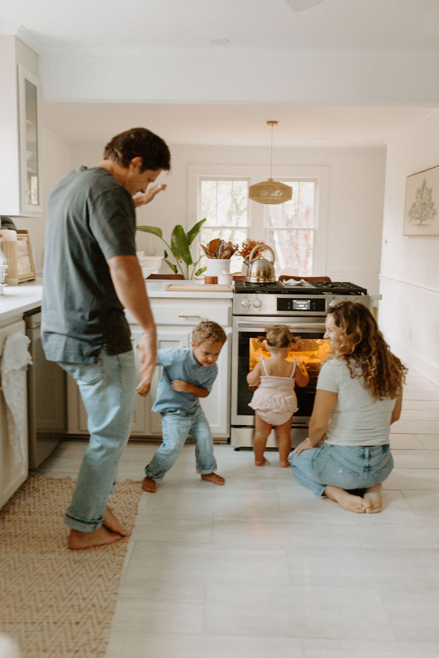 Family gathered in bright modern kitchen watching something in the oven together.