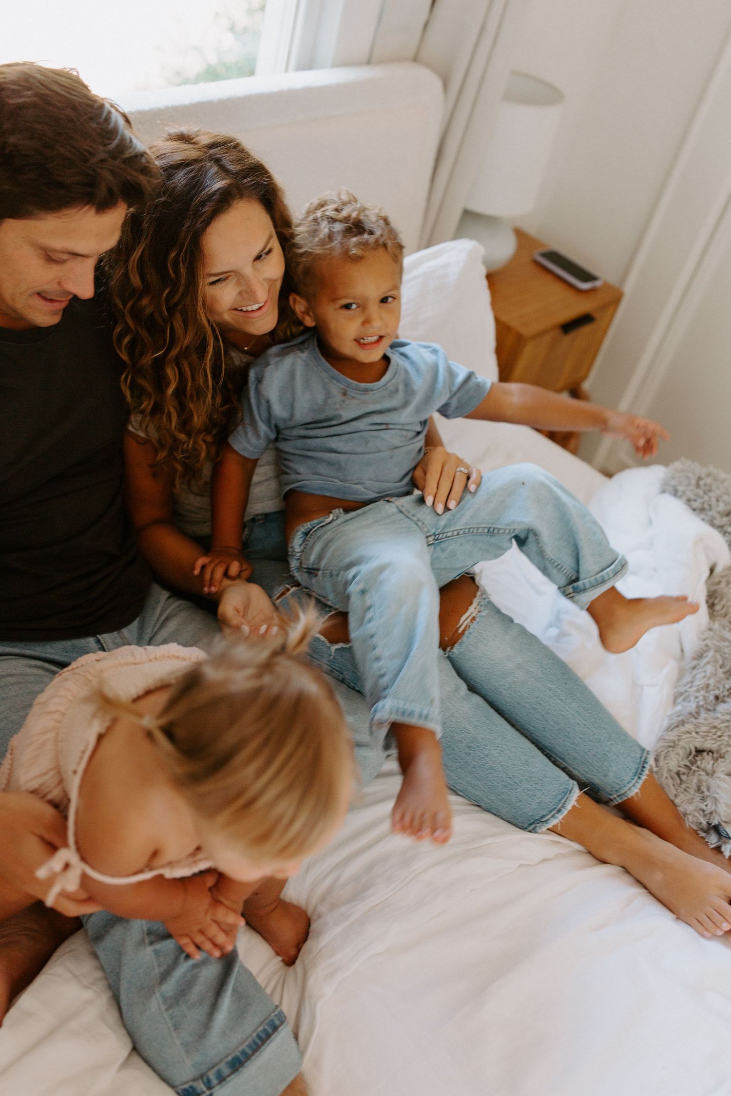 Intimate family moments captured in warm tones while relaxing on white bedding.