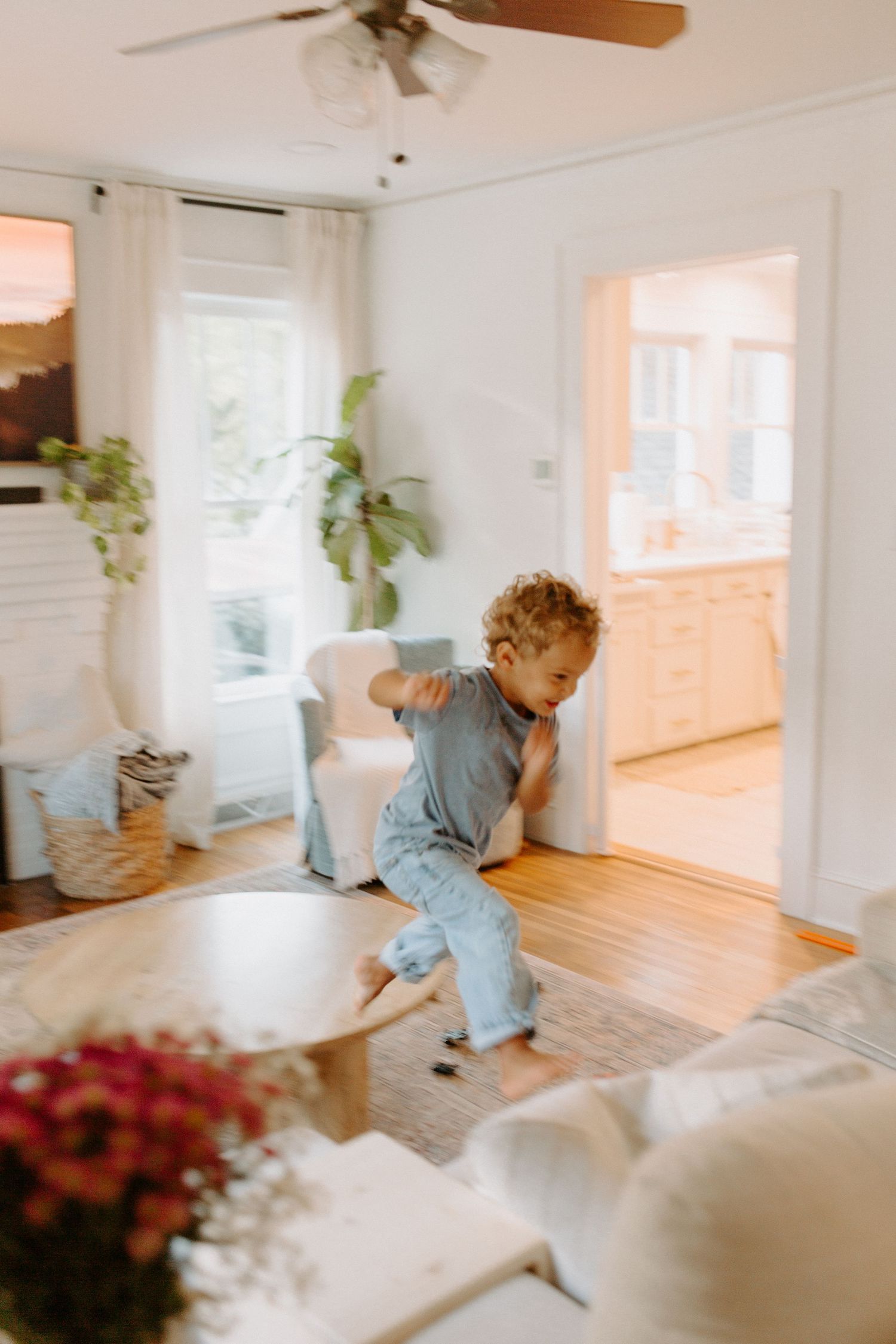 Energetic playtime captured in motion blur across a bright, airy living room with white furniture.