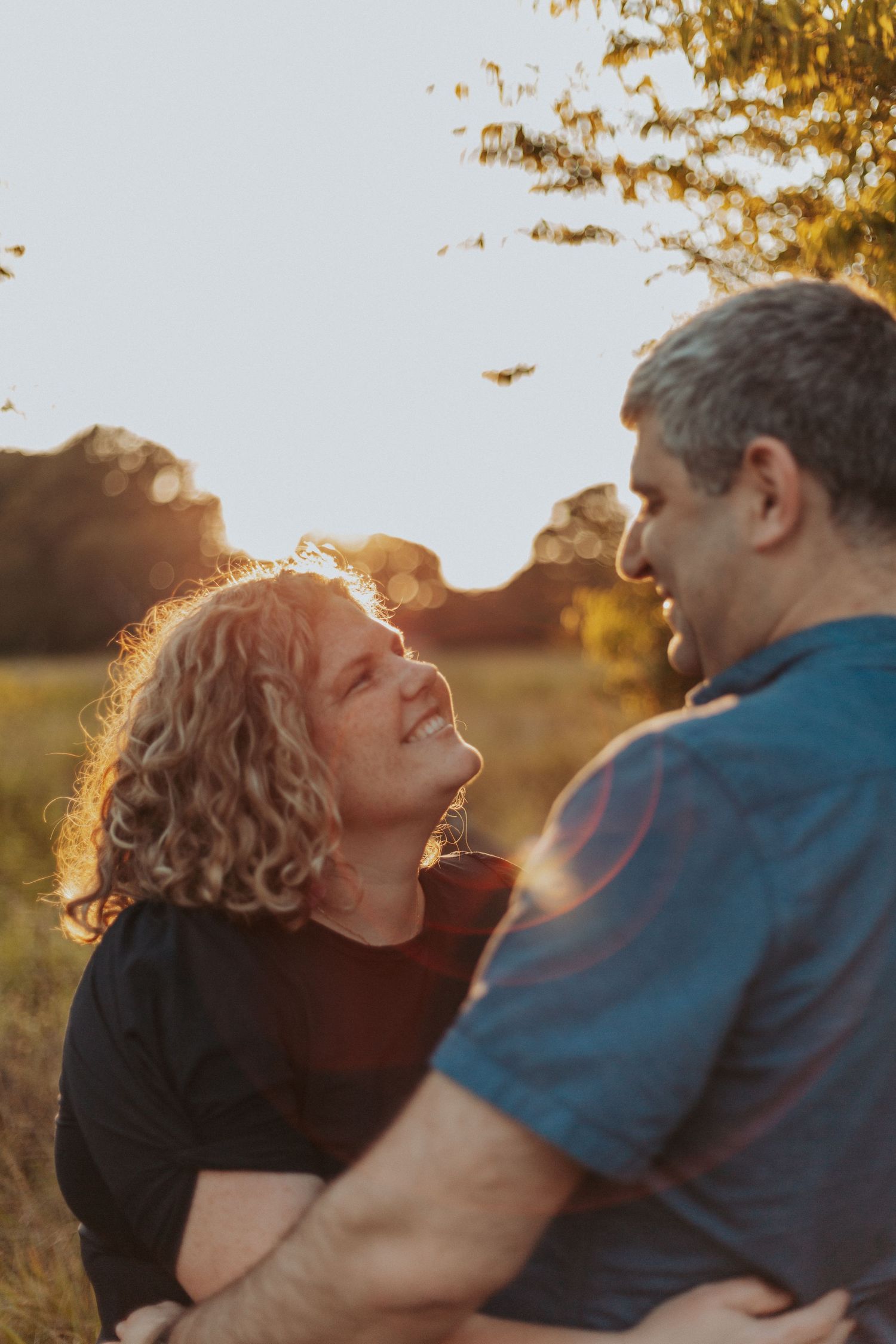 A couple shares a tender moment in warm sunset light with autumn foliage in the background.