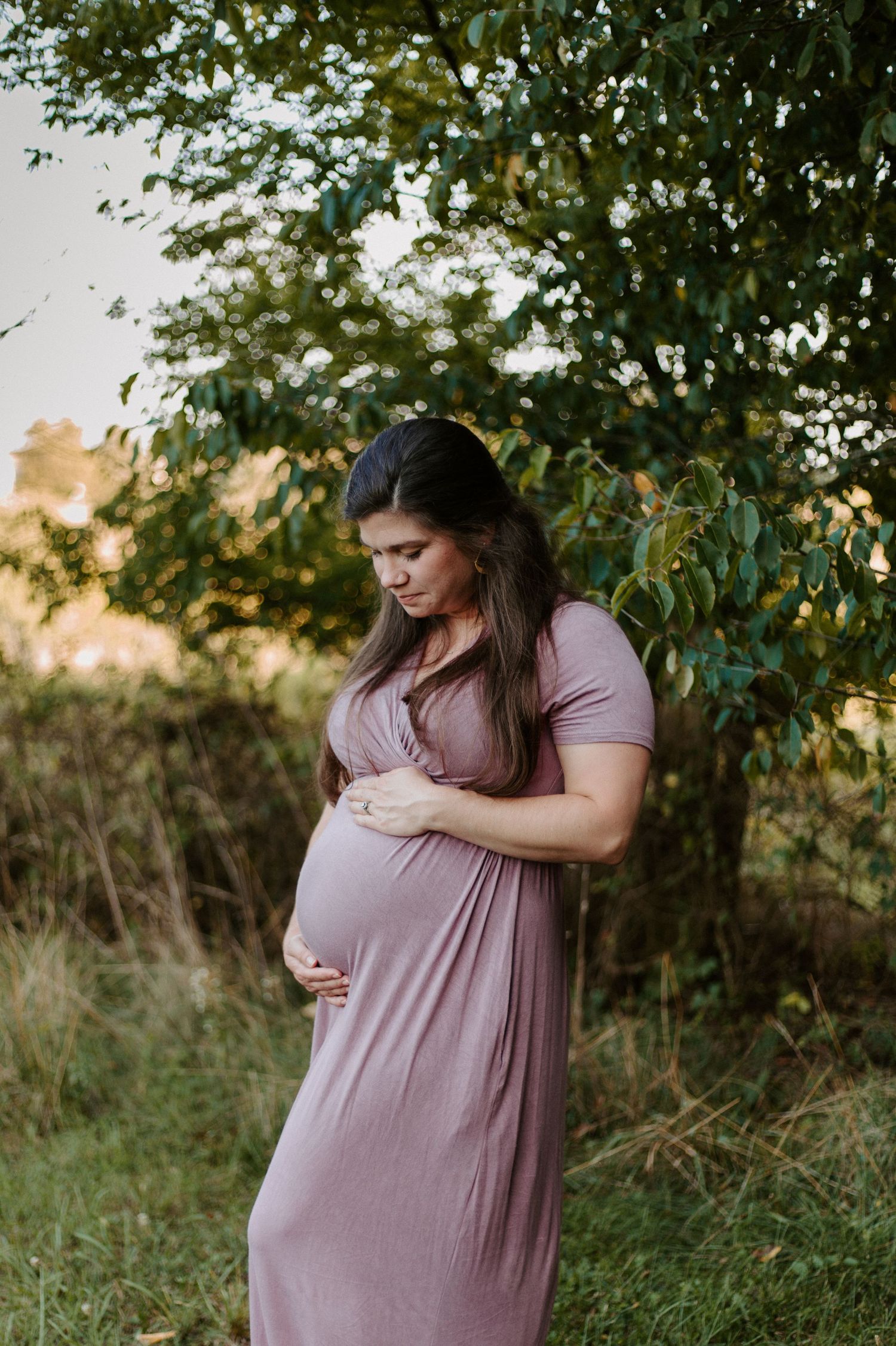 A touching maternity photo session outdoors with soft lighting and natural greenery in the background.