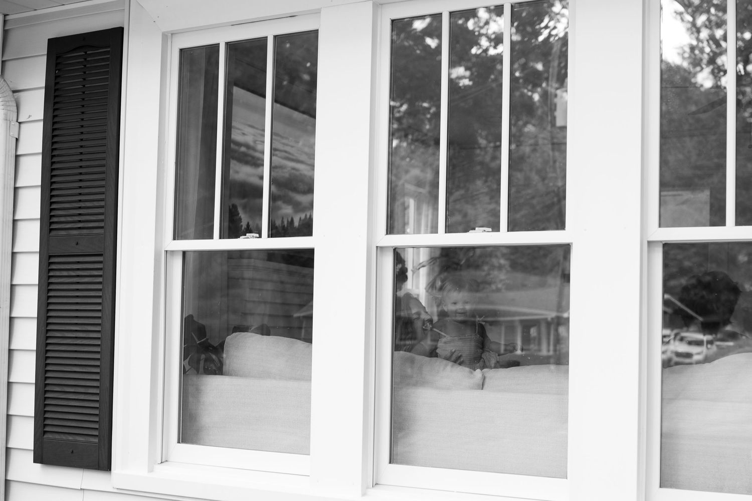 Row of large white-framed windows with black shutters on exterior of house.