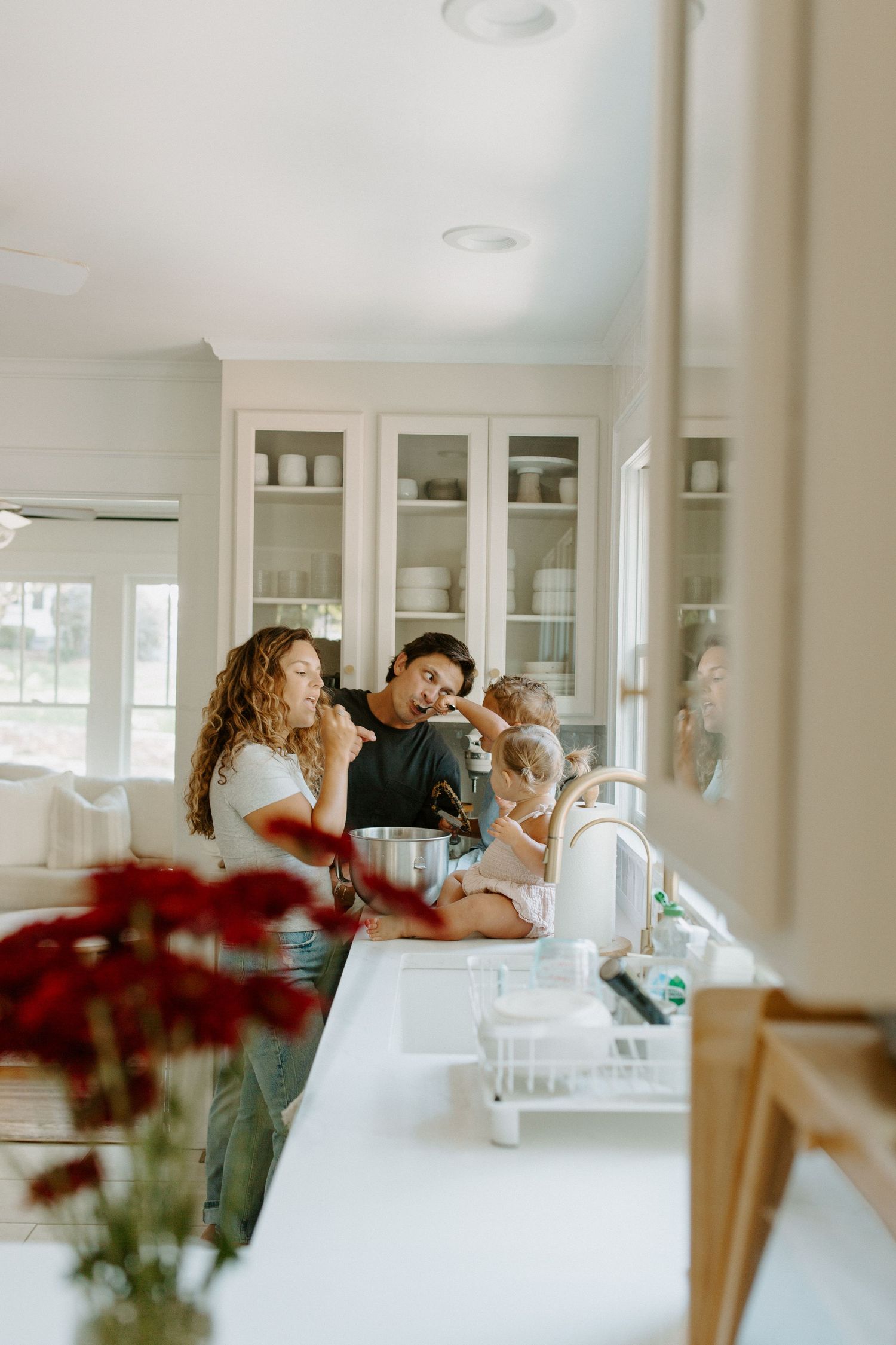 Family gathered around kitchen counter with red flowers in foreground.