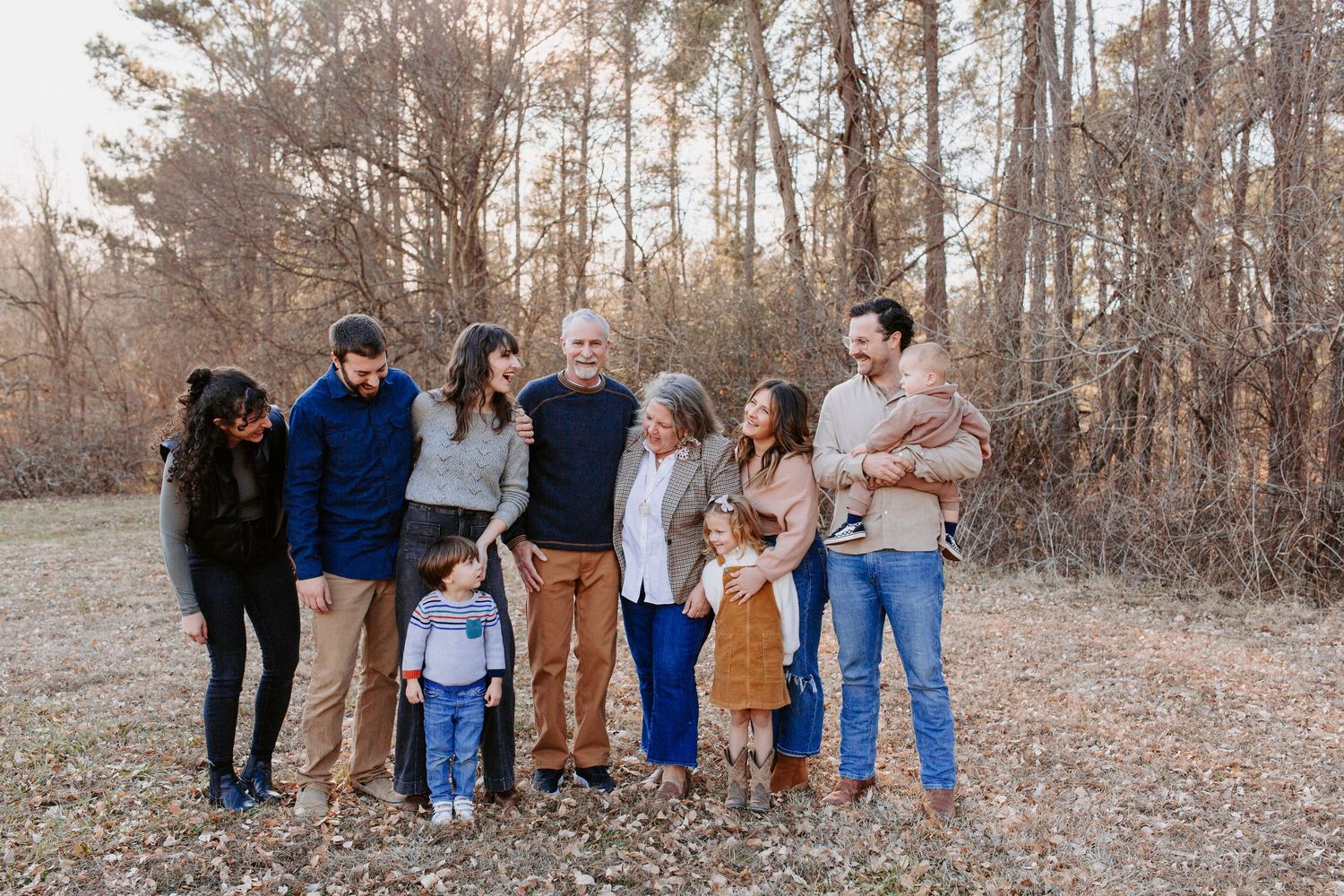 Group portrait of family members standing together outdoors in a wooded autumn setting.