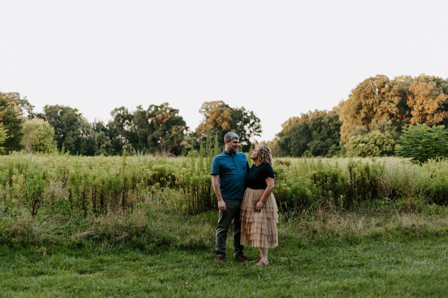 A couple walks through a scenic meadow during a countryside photo session.