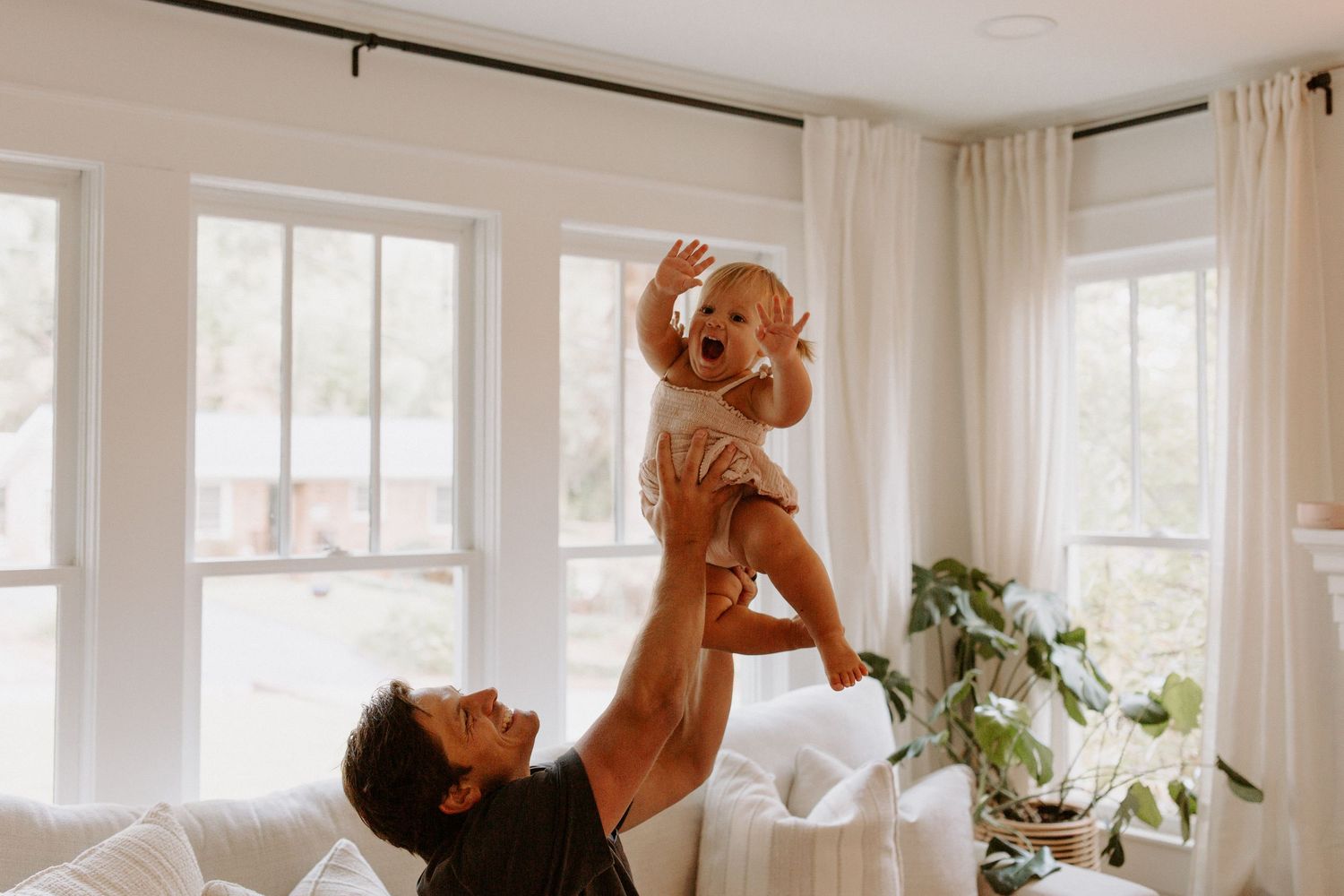 Playful moment of lifting child in bright sunlit living room.
