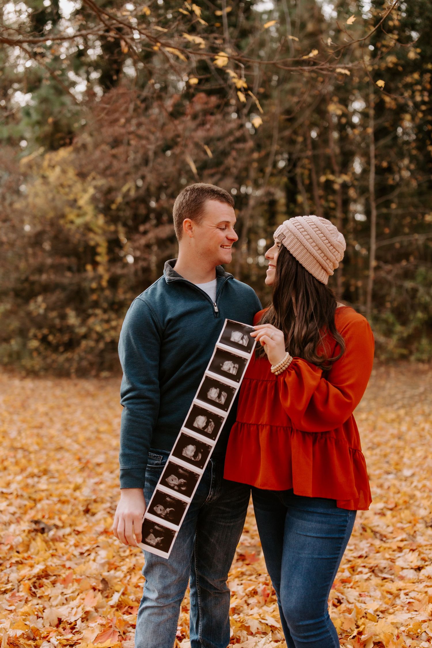A series of playful pregnancy announcement photos with ultrasound strips in a fall setting.