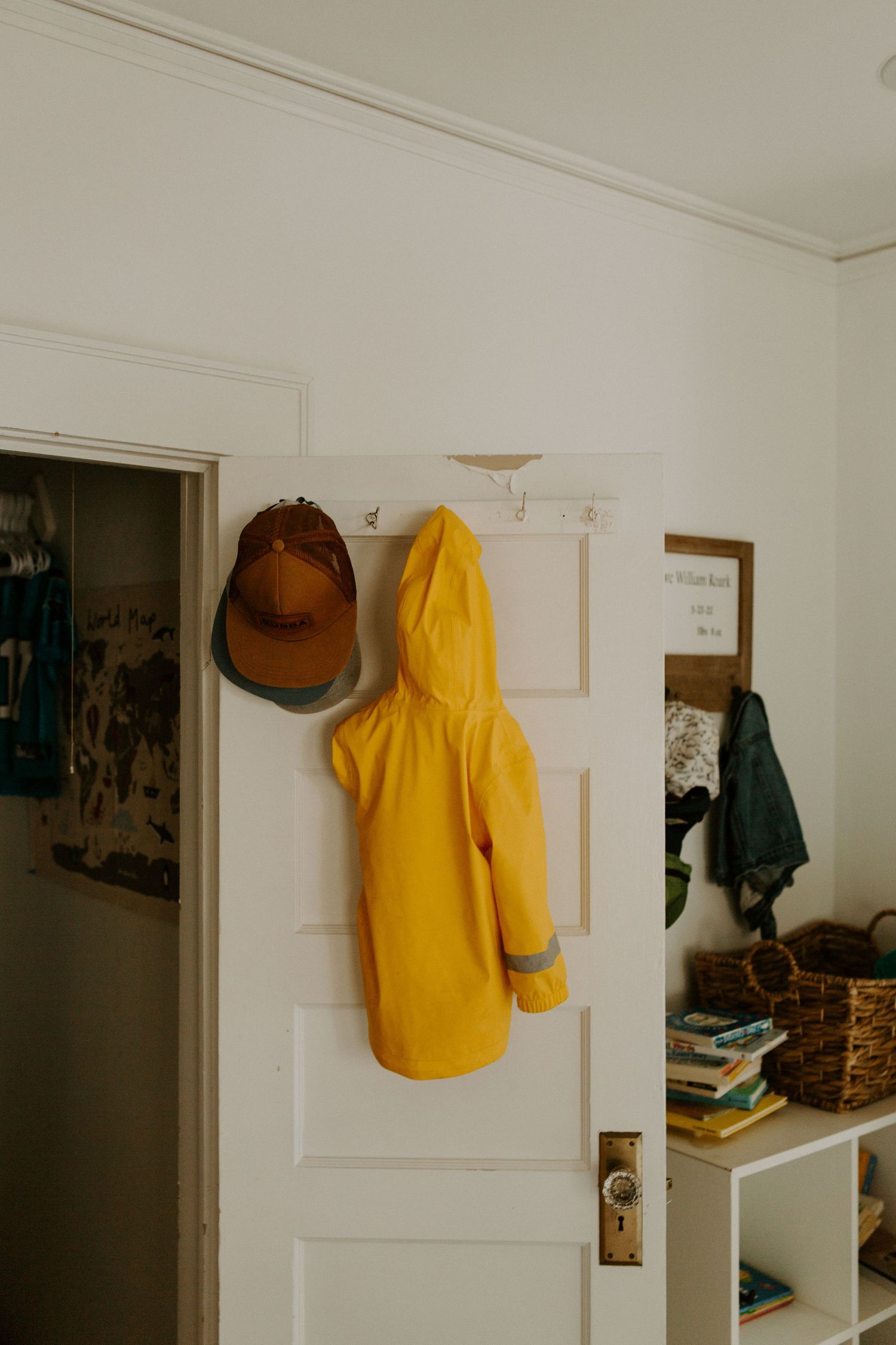 A yellow raincoat hangs on a white wall near a doorway in a minimalist interior space.