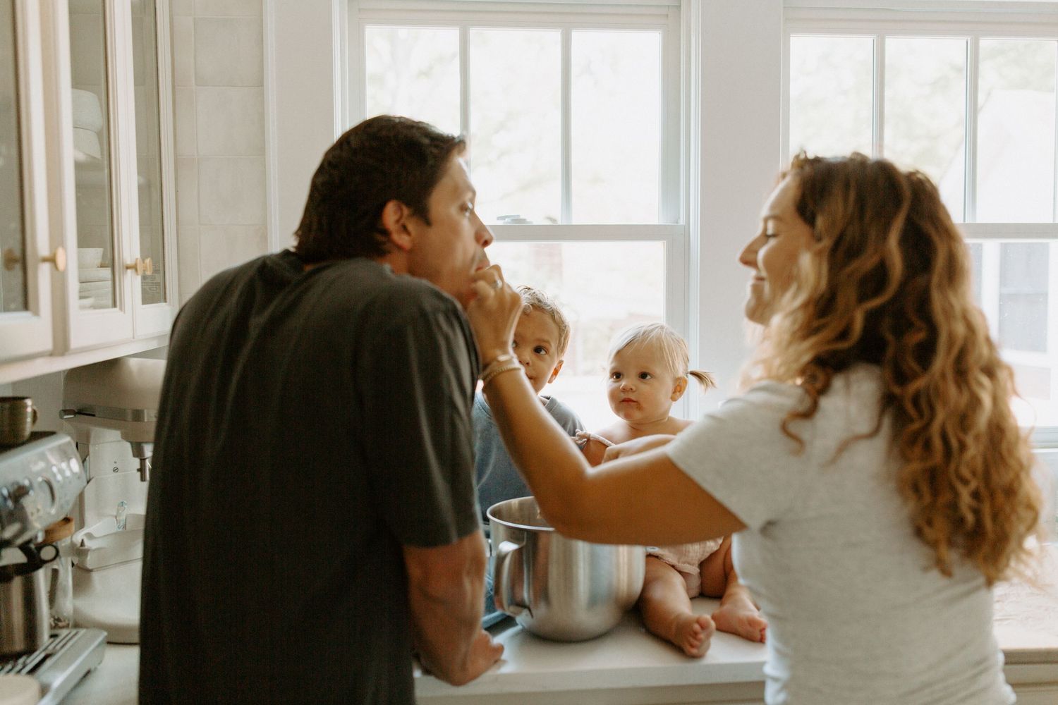 A family baking together in a bright white modern kitchen.