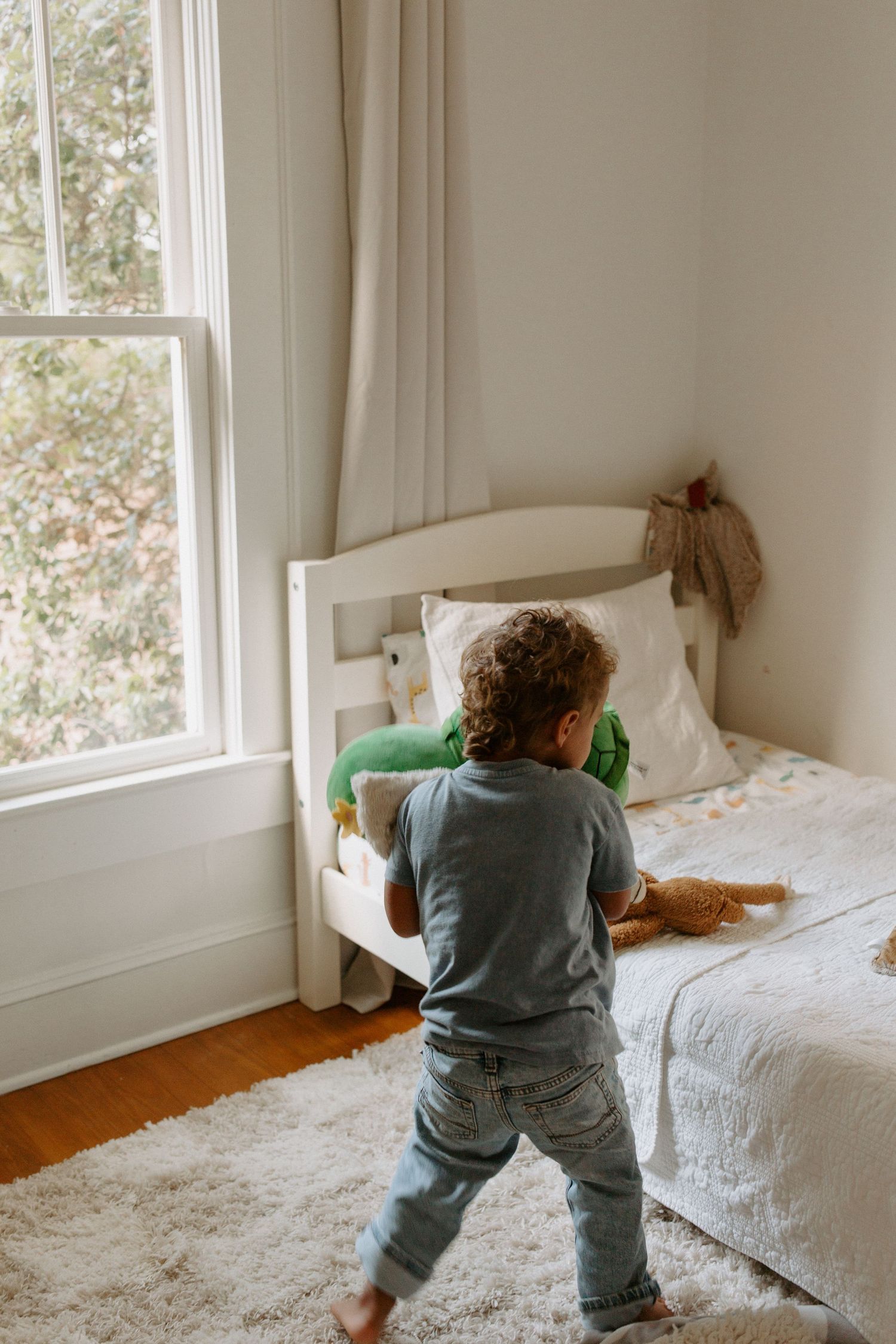 Energetic playtime captured in a bright bedroom with white bedding and natural light.