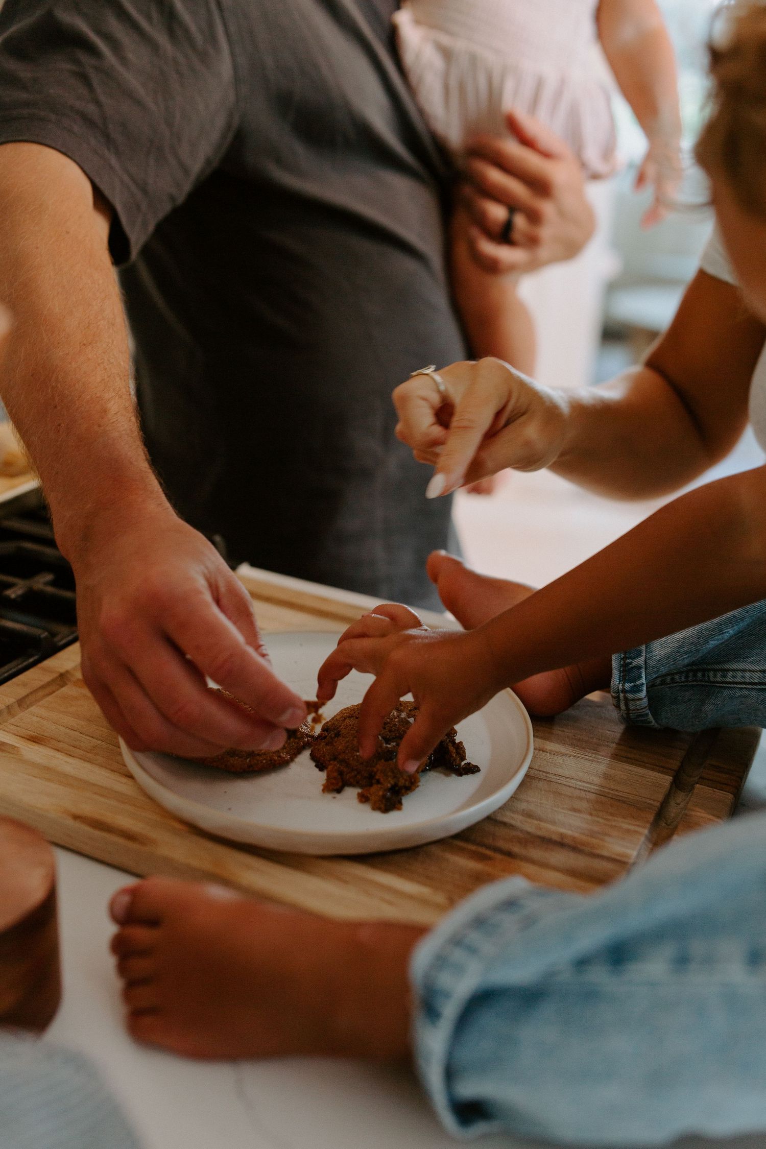 Close-up of hands sharing food on a white plate in a kitchen setting.