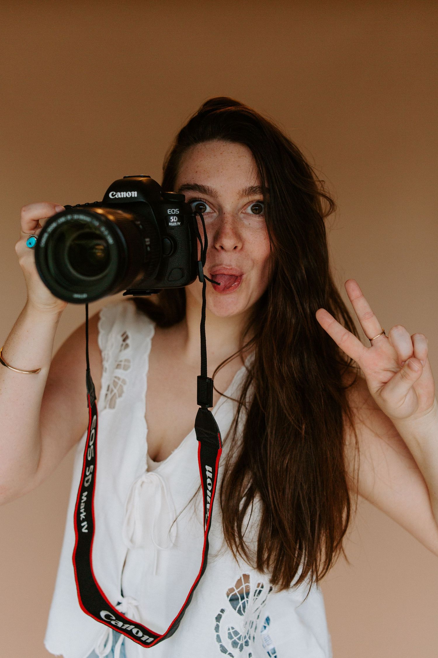 Photographer taking selfie with Canon DSLR camera while making peace sign.