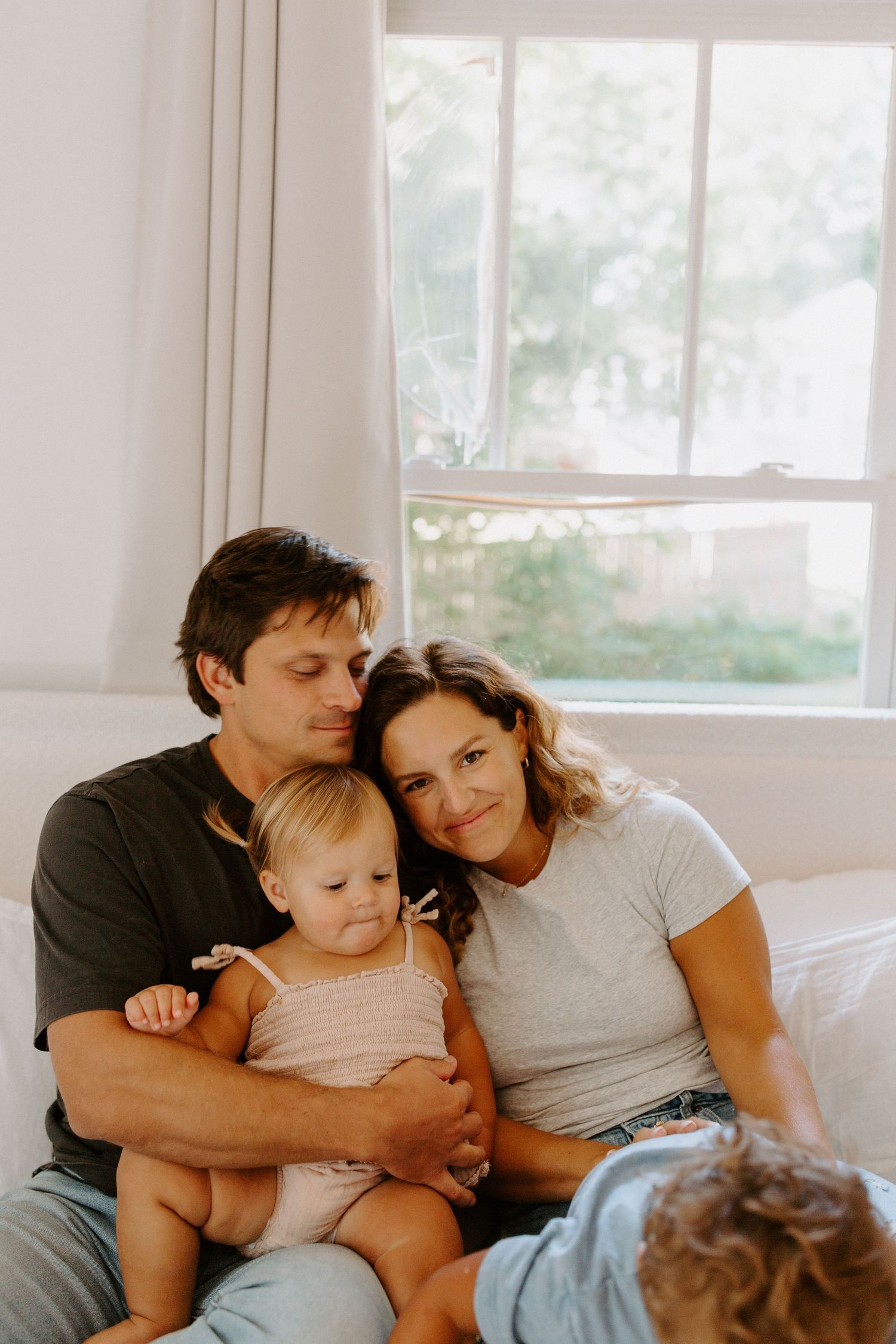 A tender family moment captured in warm sunlight streaming through a bedroom window.