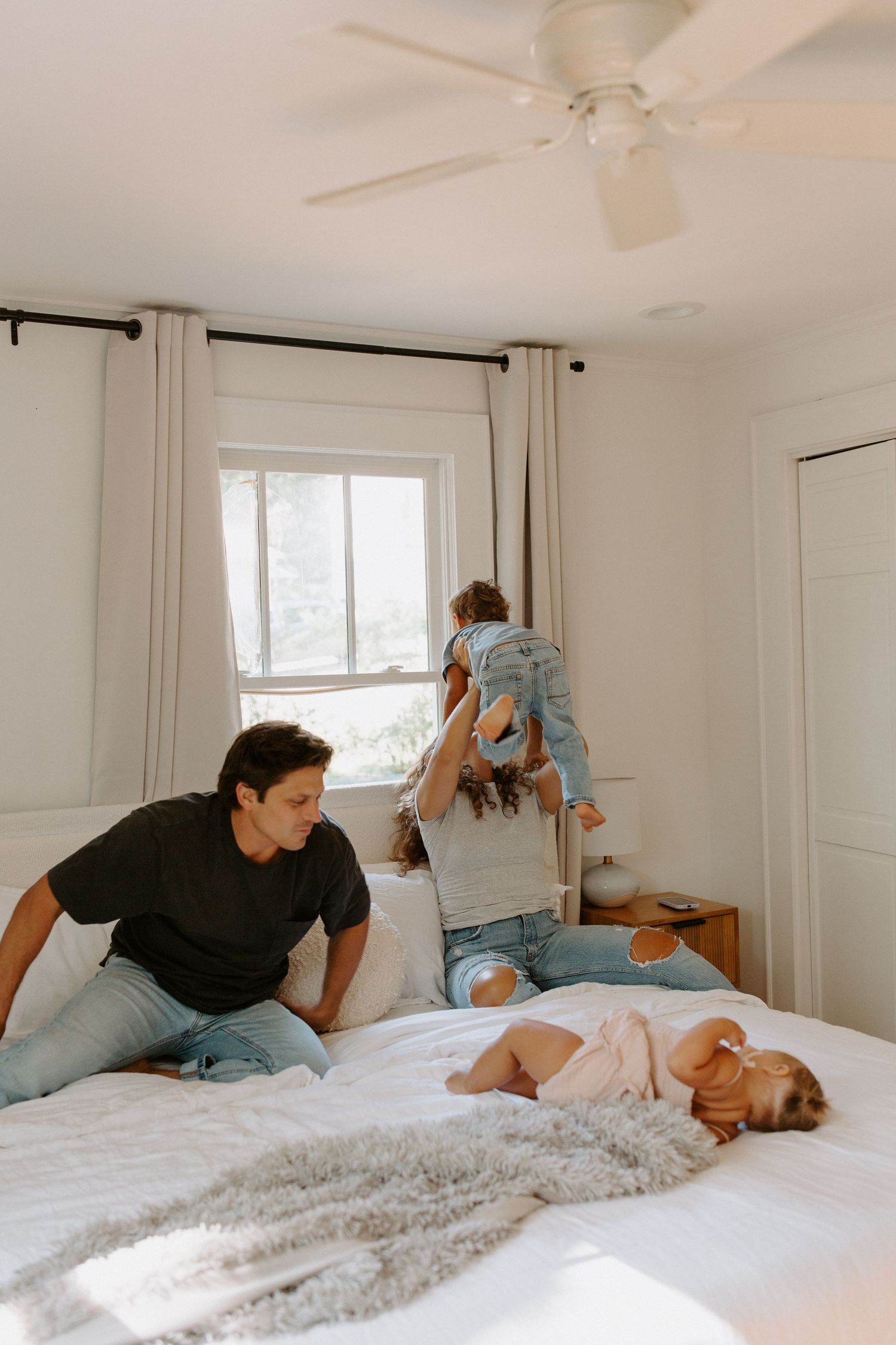Playful family interaction on a comfortable bed with white bedding and curtains.