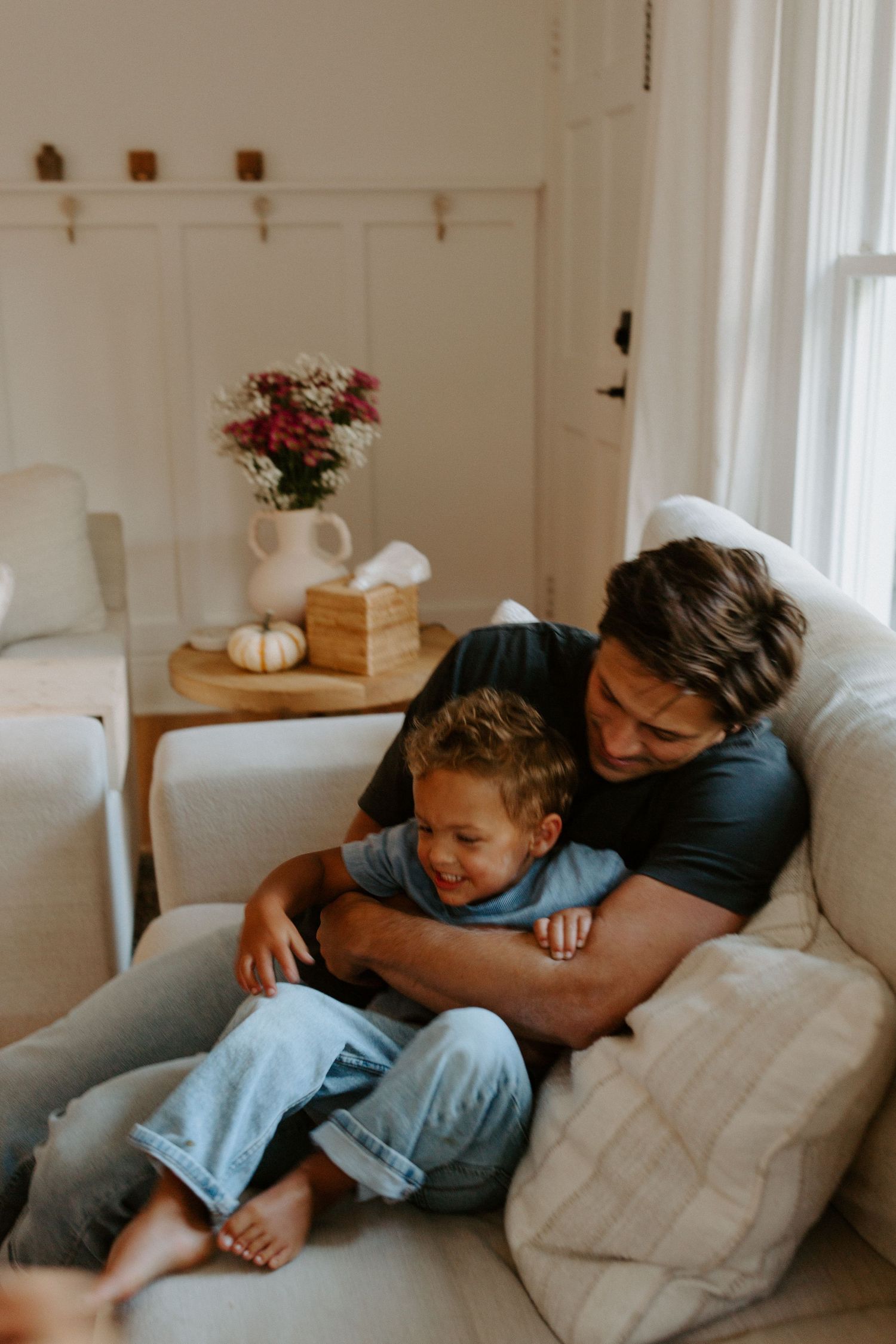 Playful moments captured on a comfortable gray sofa with natural window light streaming in.