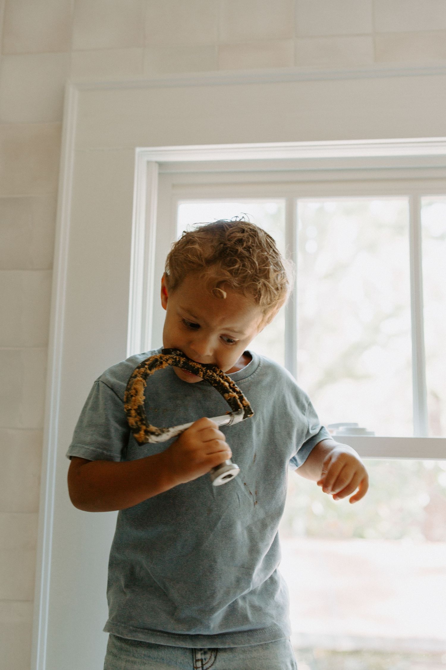 Young child enjoying a snack while sitting on kitchen counter near window.