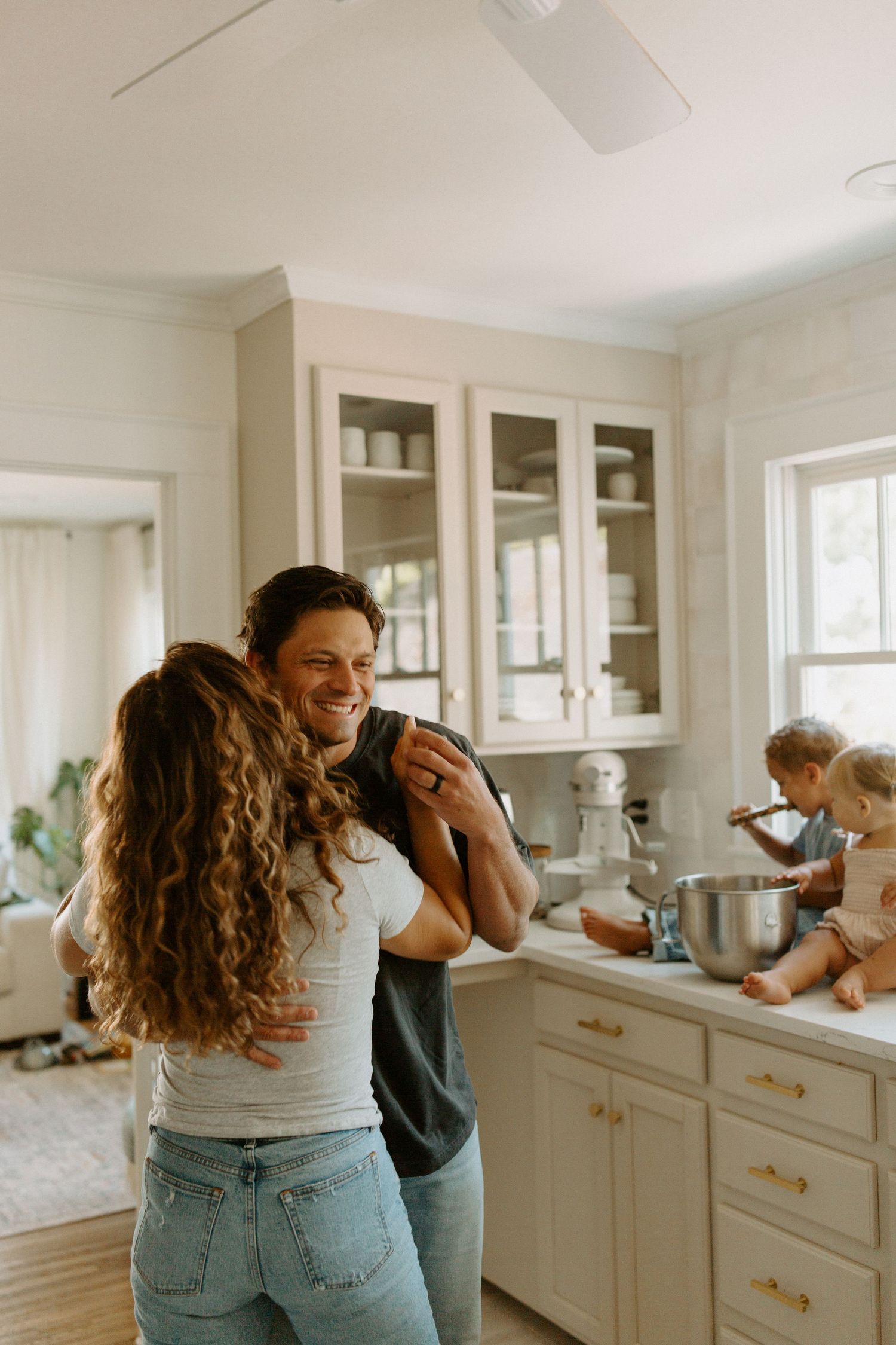 Joyful kitchen scene with family members laughing and embracing by white cabinets.