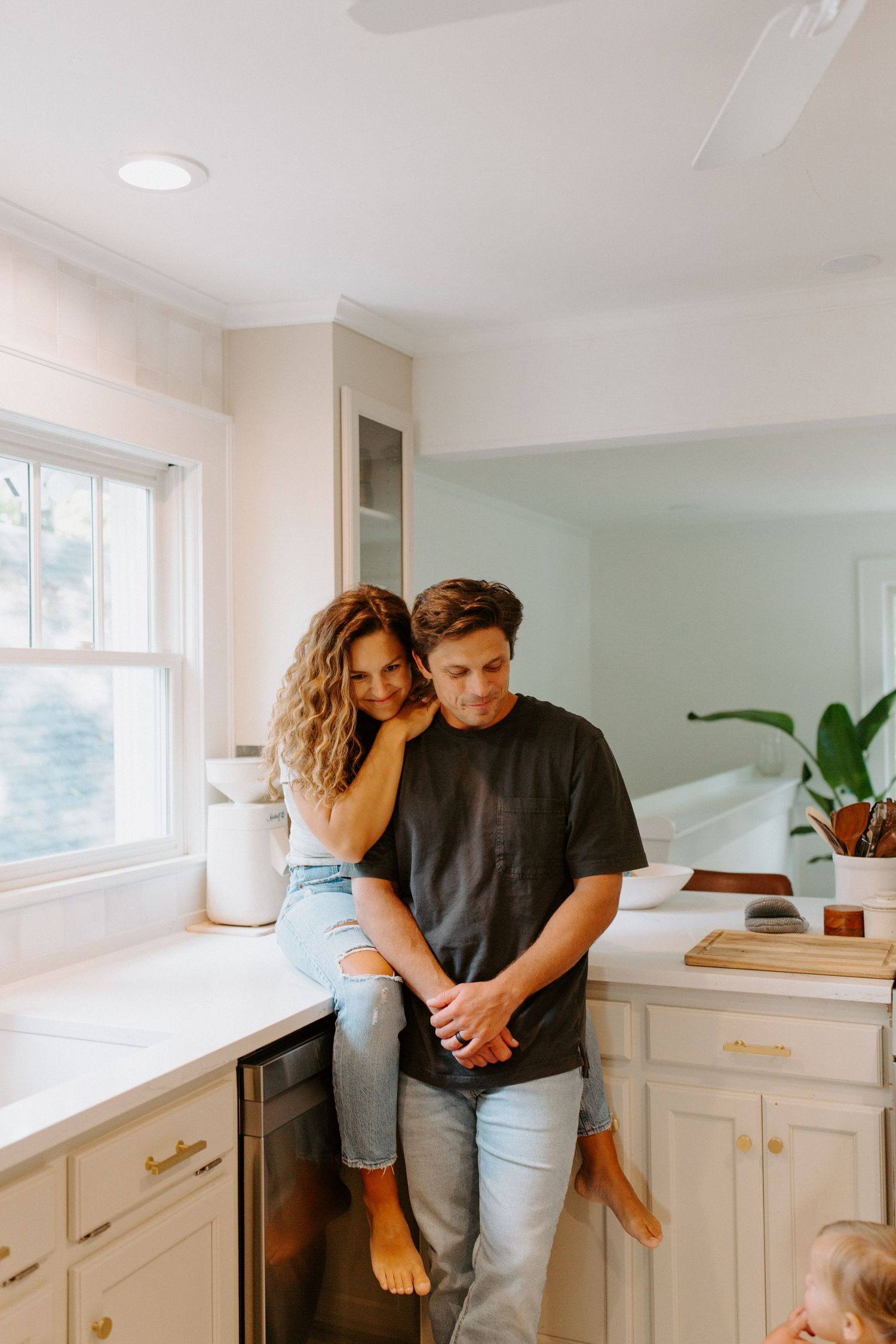 A couple shares intimate moments in a bright white kitchen with mint green walls and modern cabinetry.
