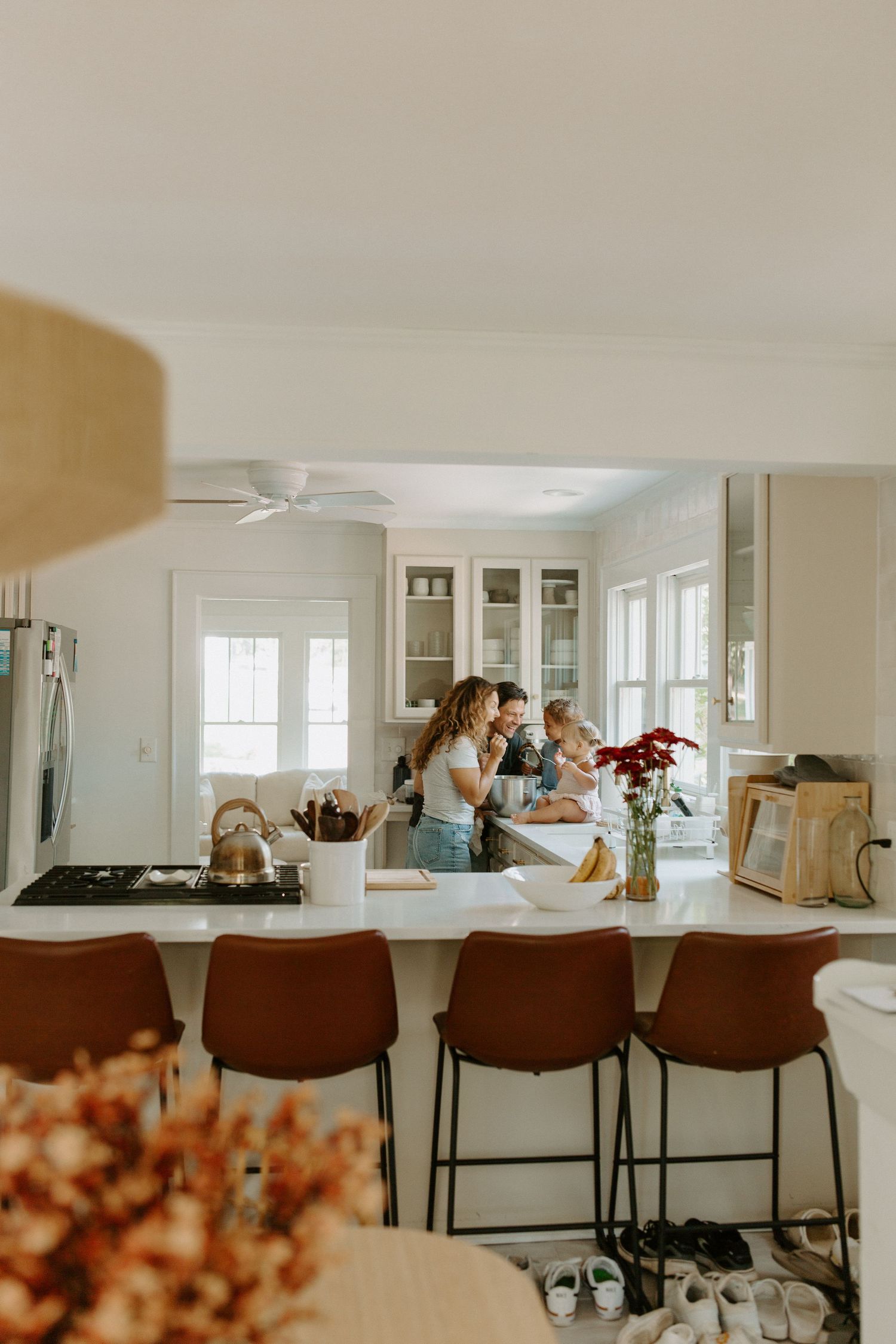 Modern white kitchen with brown barstools and natural light streaming through windows.
