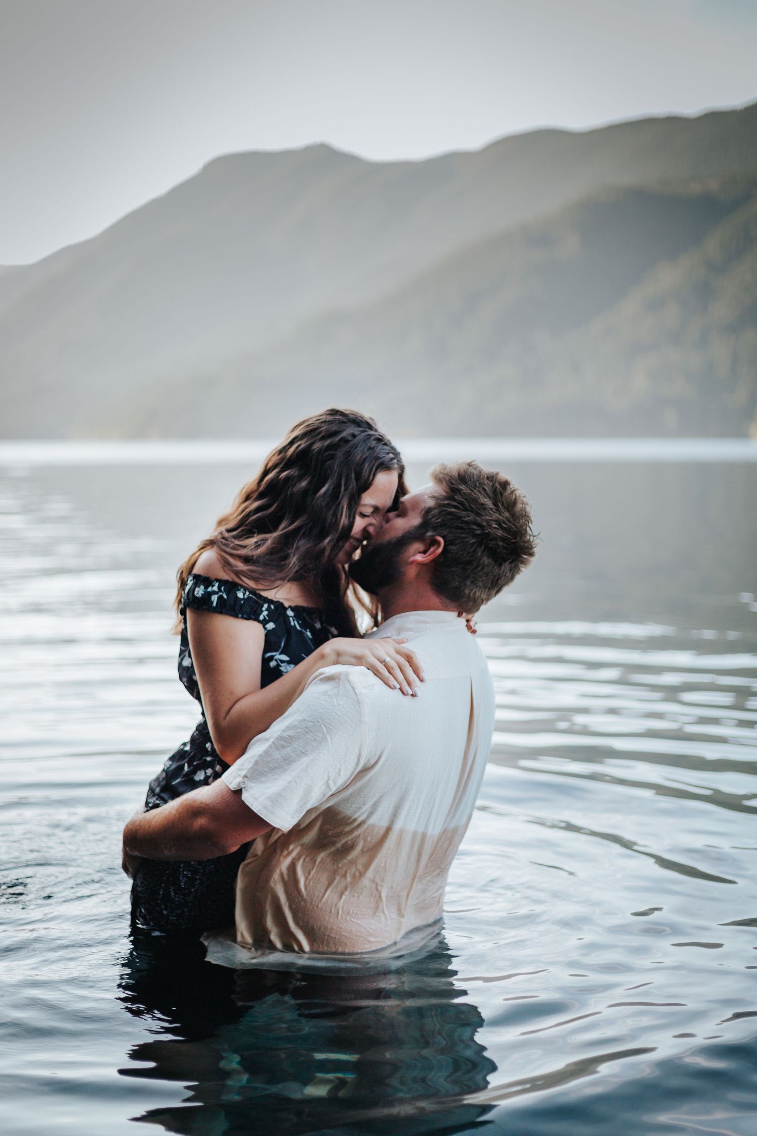 A romantic couple embraces while standing in a misty mountain lake during a photo session.