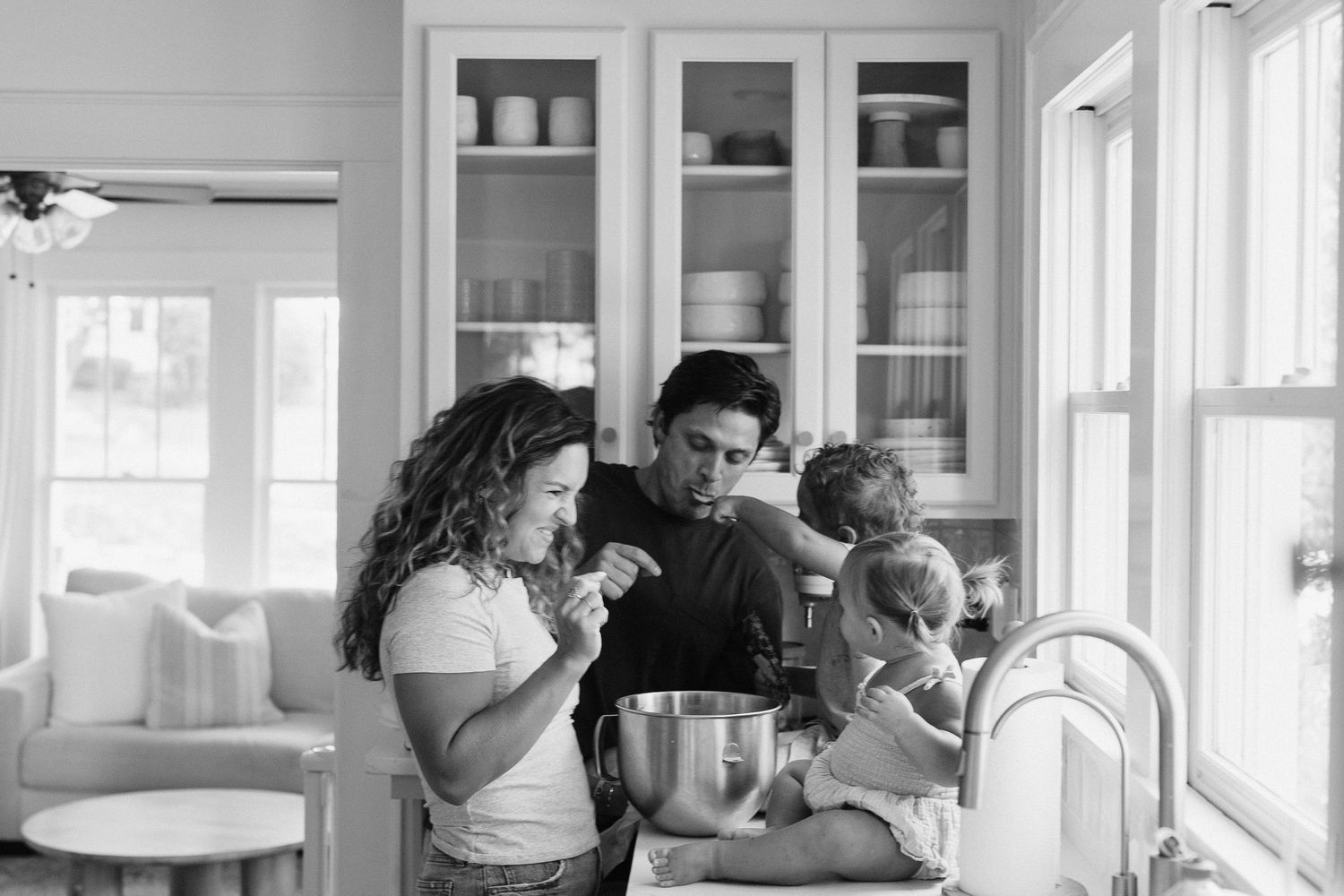 Sunlit kitchen scene with family members gathered by counter.