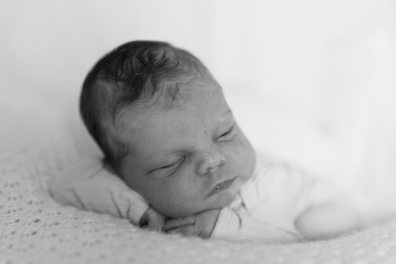 Serene black and white portrait of sleeping newborn on white backdrop.