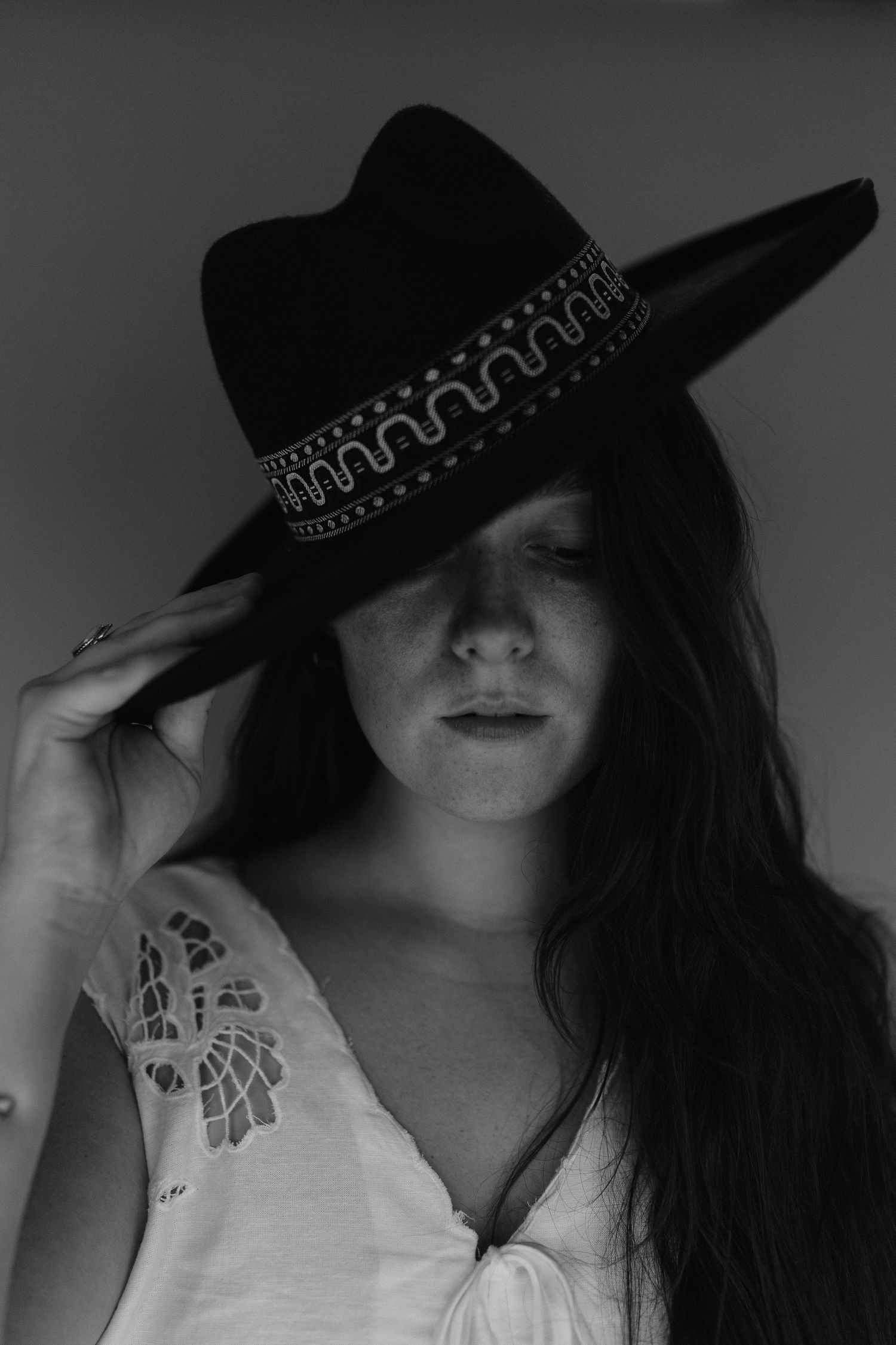 Dramatic black and white portrait of woman wearing decorative hat and white top.