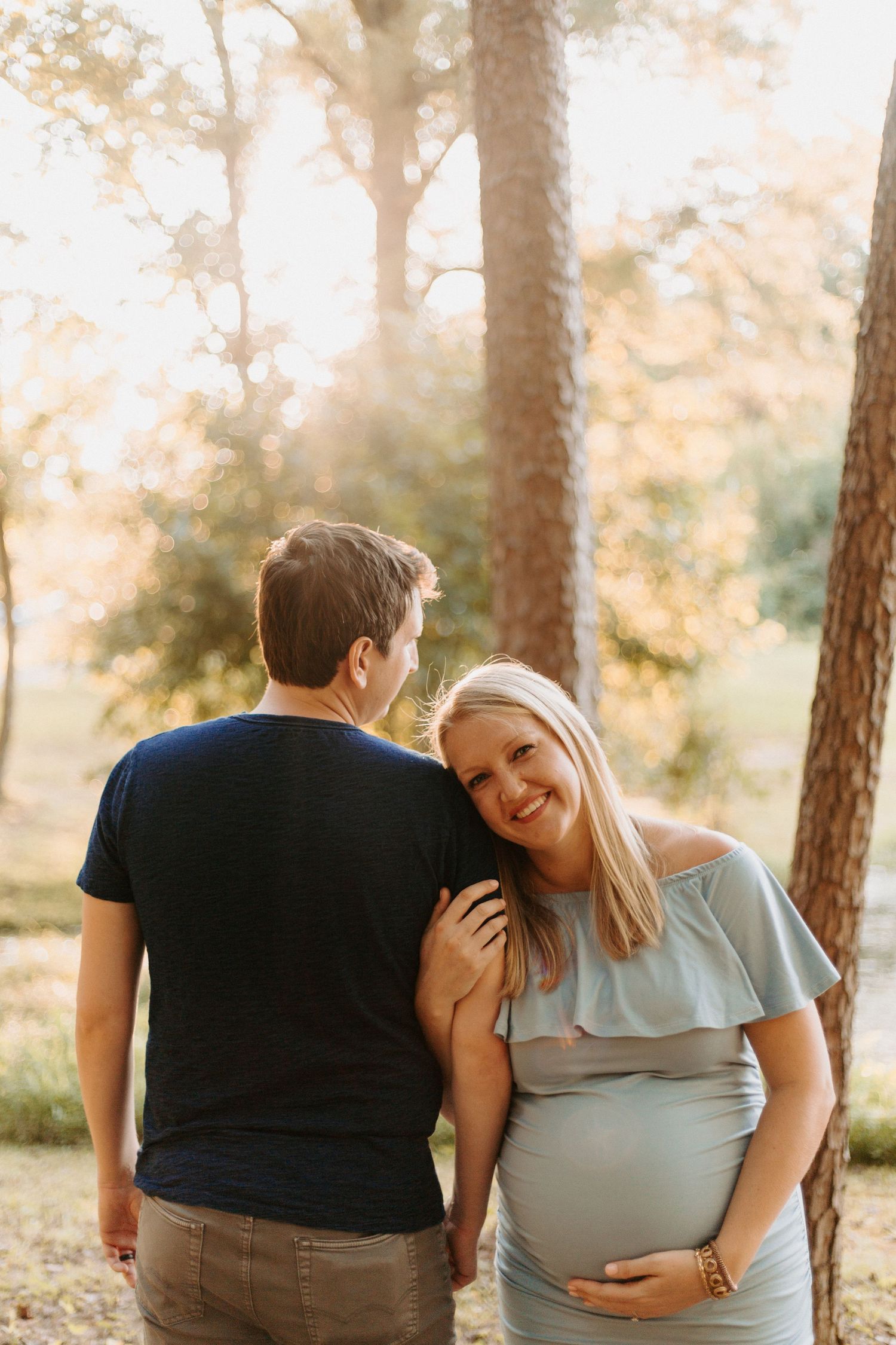 A series of candid pregnancy announcement photos taken in a sun-drenched pine forest.