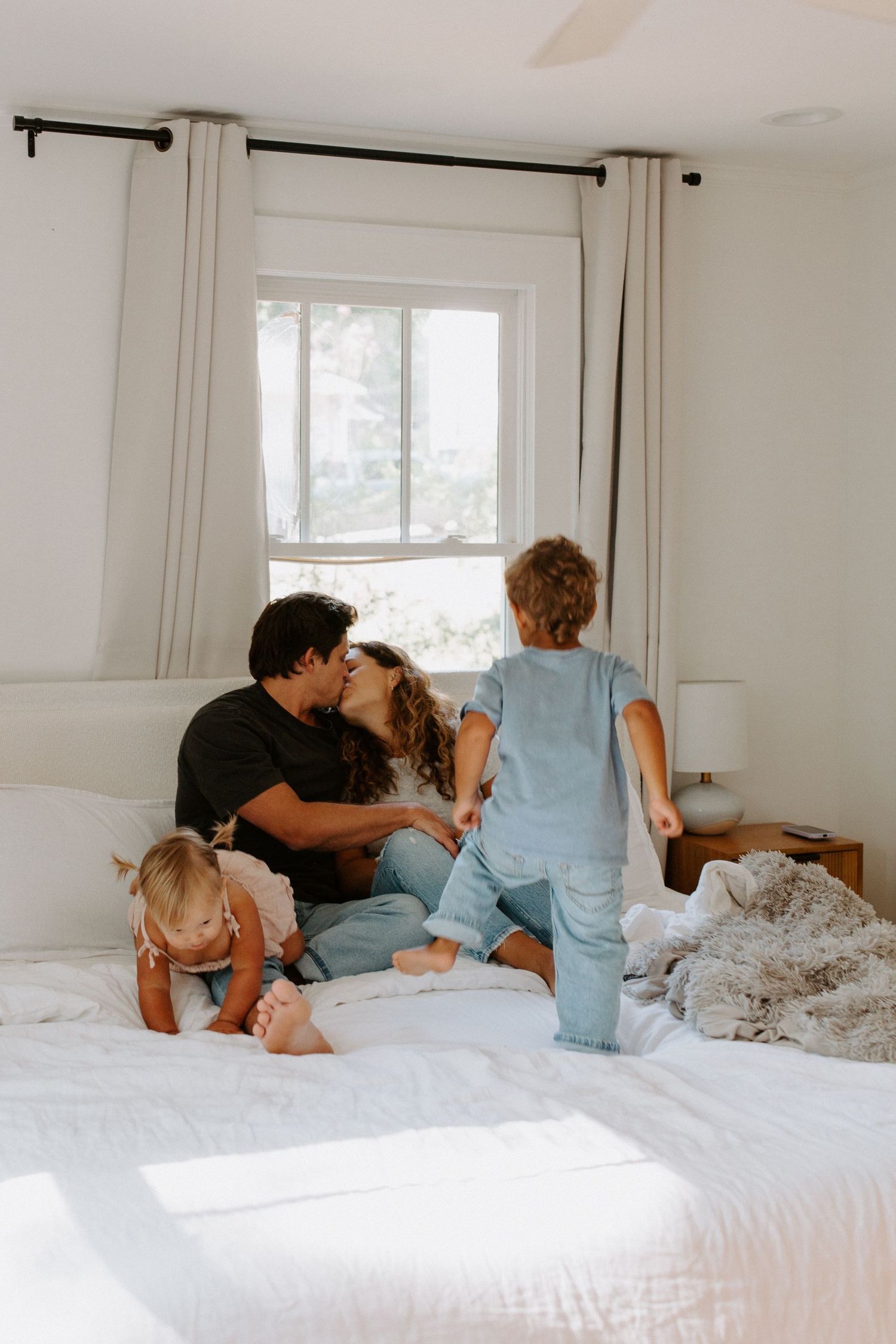 Candid moments of family affection captured on a bright white bed with blue pillows.