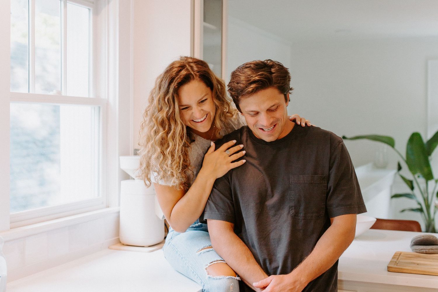 A couple shares an intimate moment in a bright modern kitchen with white cabinets and natural lighting.