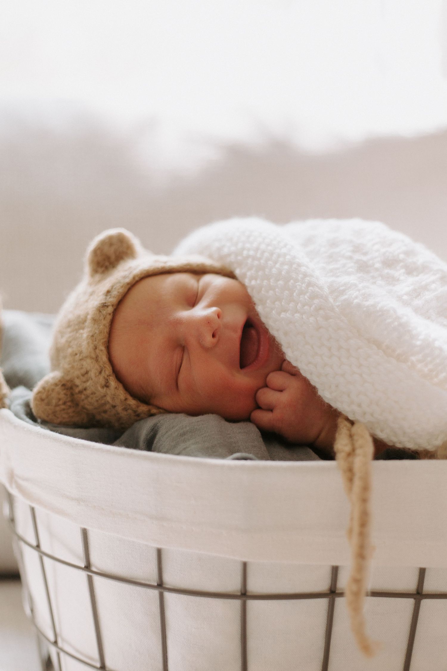 Newborn baby sleeping in white vintage basket with knit blanket.