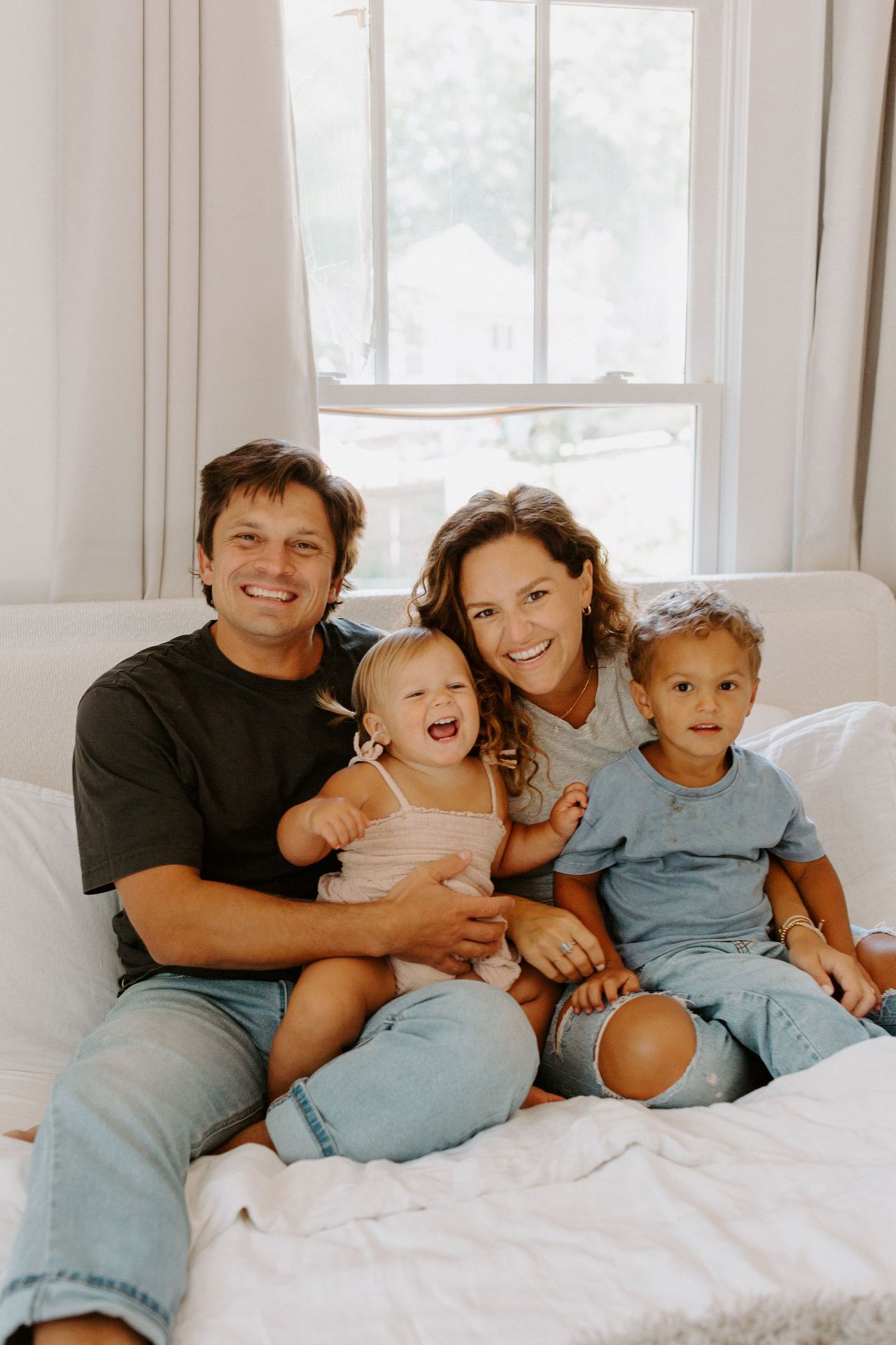 A joyful family photo session showing genuine smiles and laughter on a white bed.