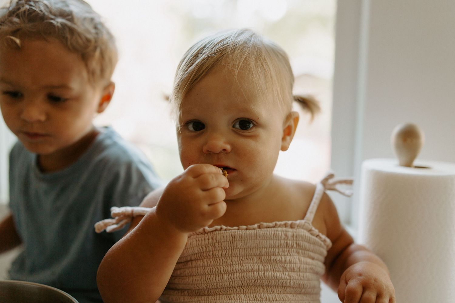 Two children watching curiously as baking happens in a bright kitchen.