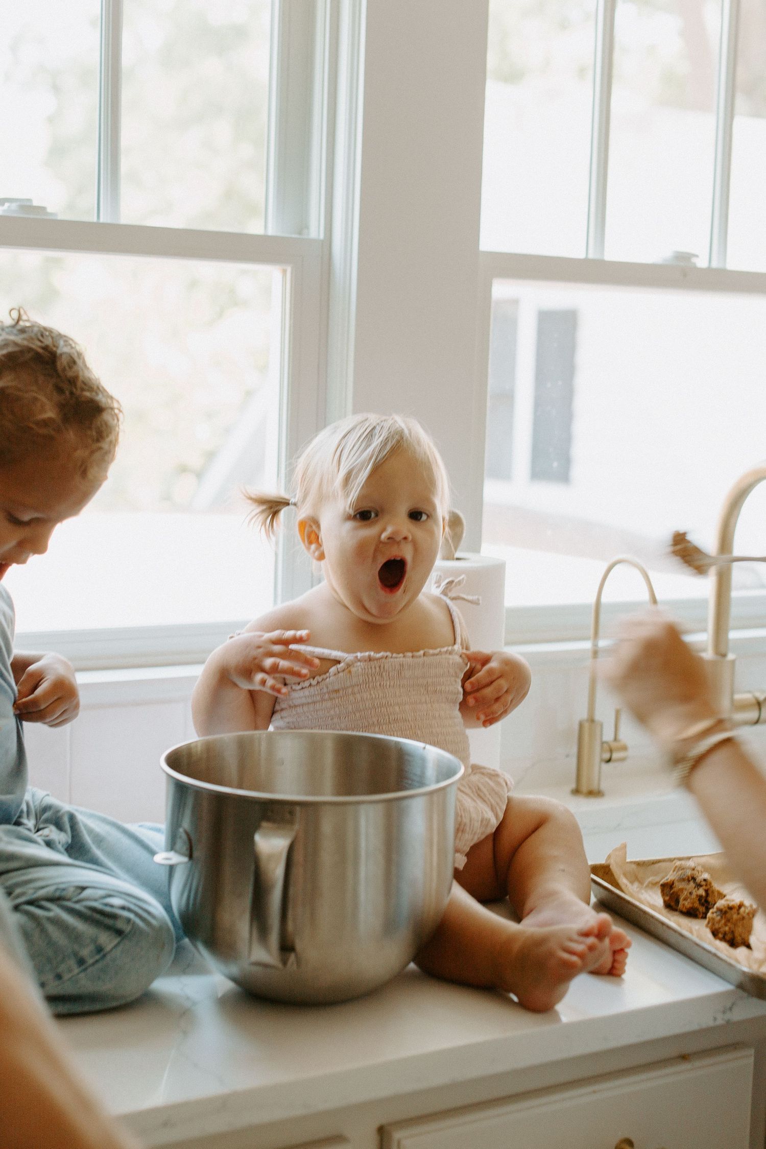 Little one sitting on kitchen counter exploring ingredients in mixing bowl.