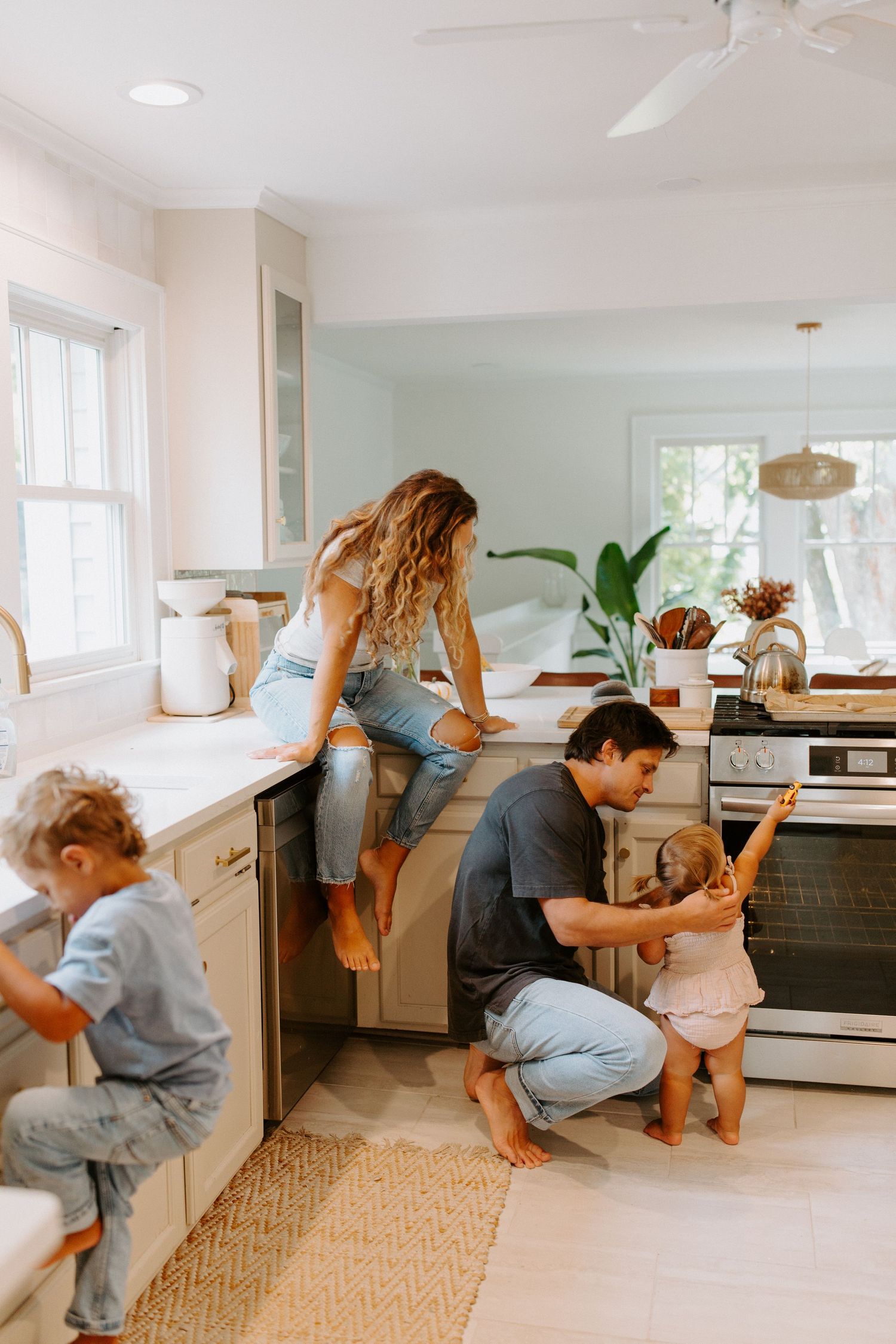 A playful family moment unfolds in a contemporary kitchen with white cabinets and natural lighting.