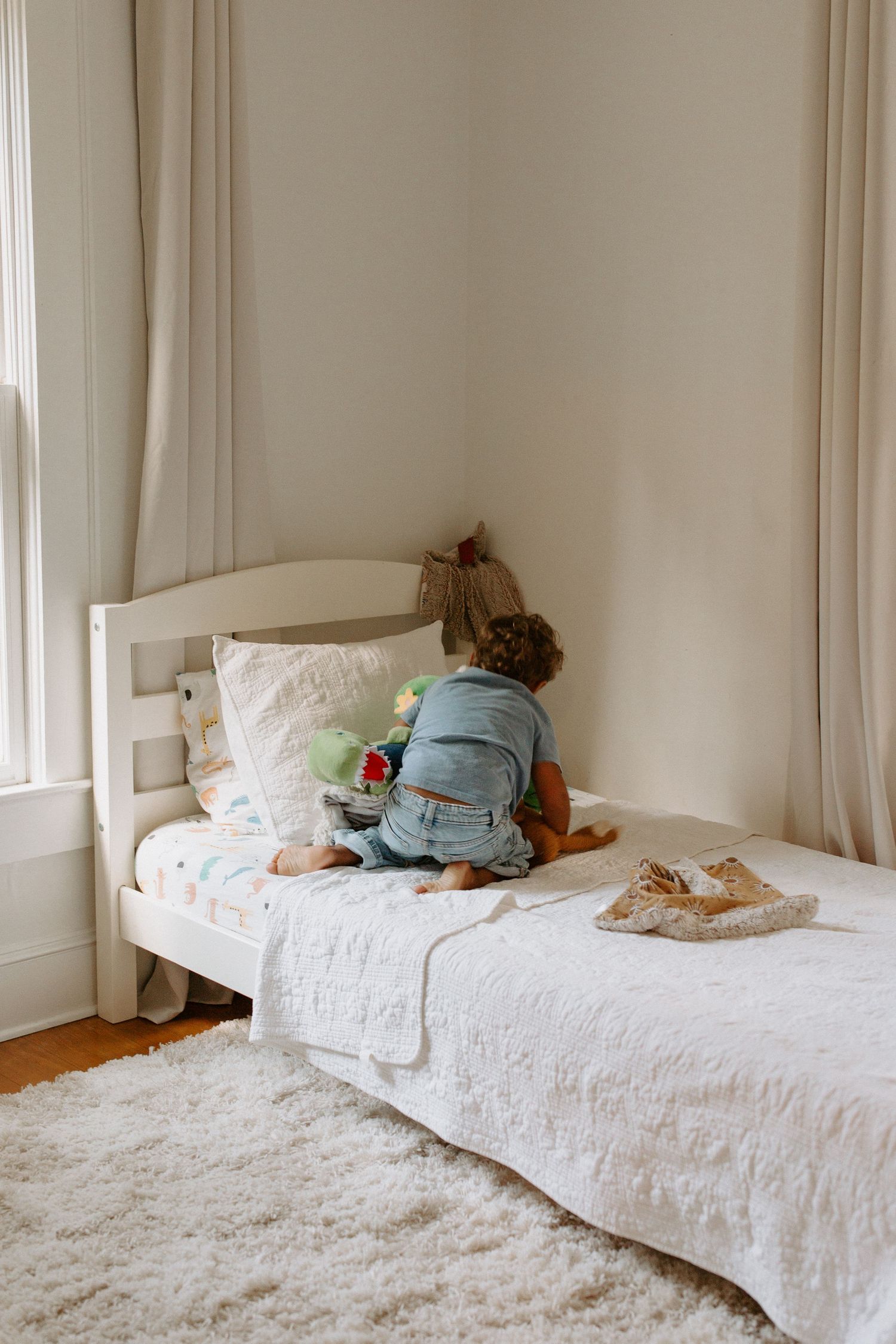 White bedding and pillows arranged on a comfortable bed next to a bright window.