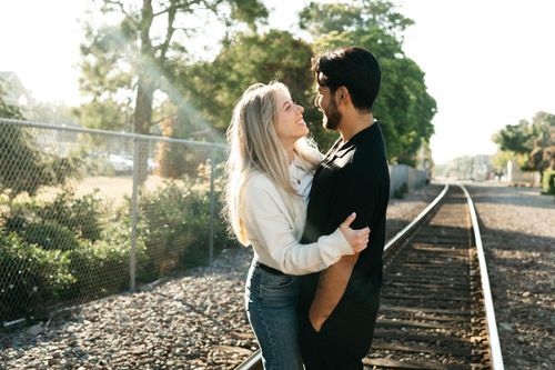 Romantic couple posing together on outdoor path with trees in background.