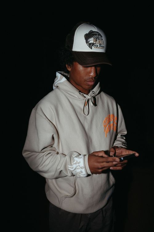 Guy looking down at his phone in a hoodie and hat.
