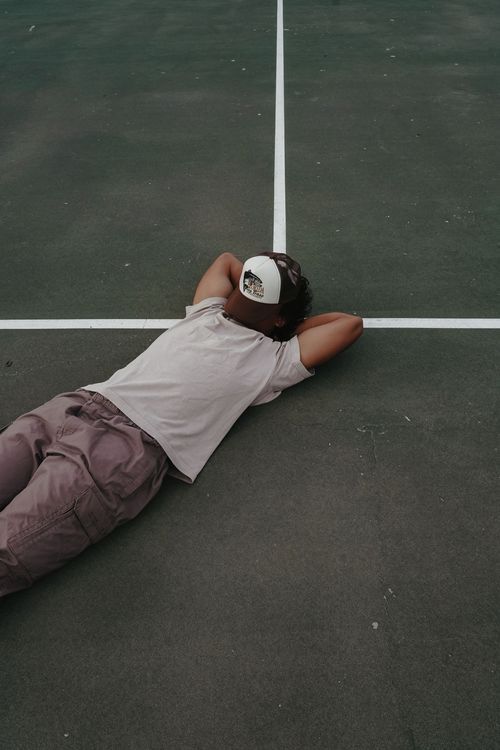Person lying down on dark basketball court surface wearing casual clothing.