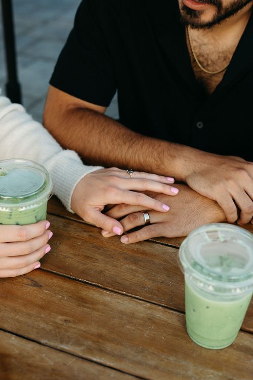 Close-up of hands on wooden table with matcha in clear plastic cup.