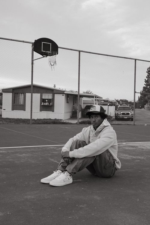 Person resting on outdoor basketball court with fence and buildings in background.