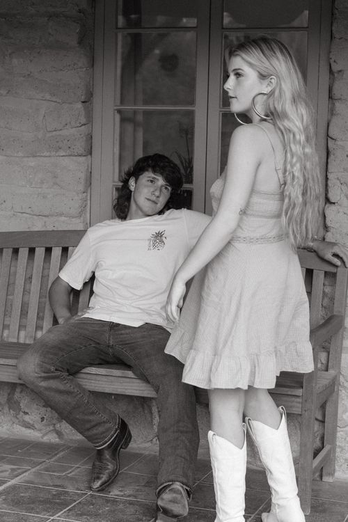 Couple in white dress and dark clothes posing playfully on porch steps.