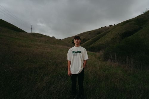 Guy standing in the middle of hills in a white t shirt.