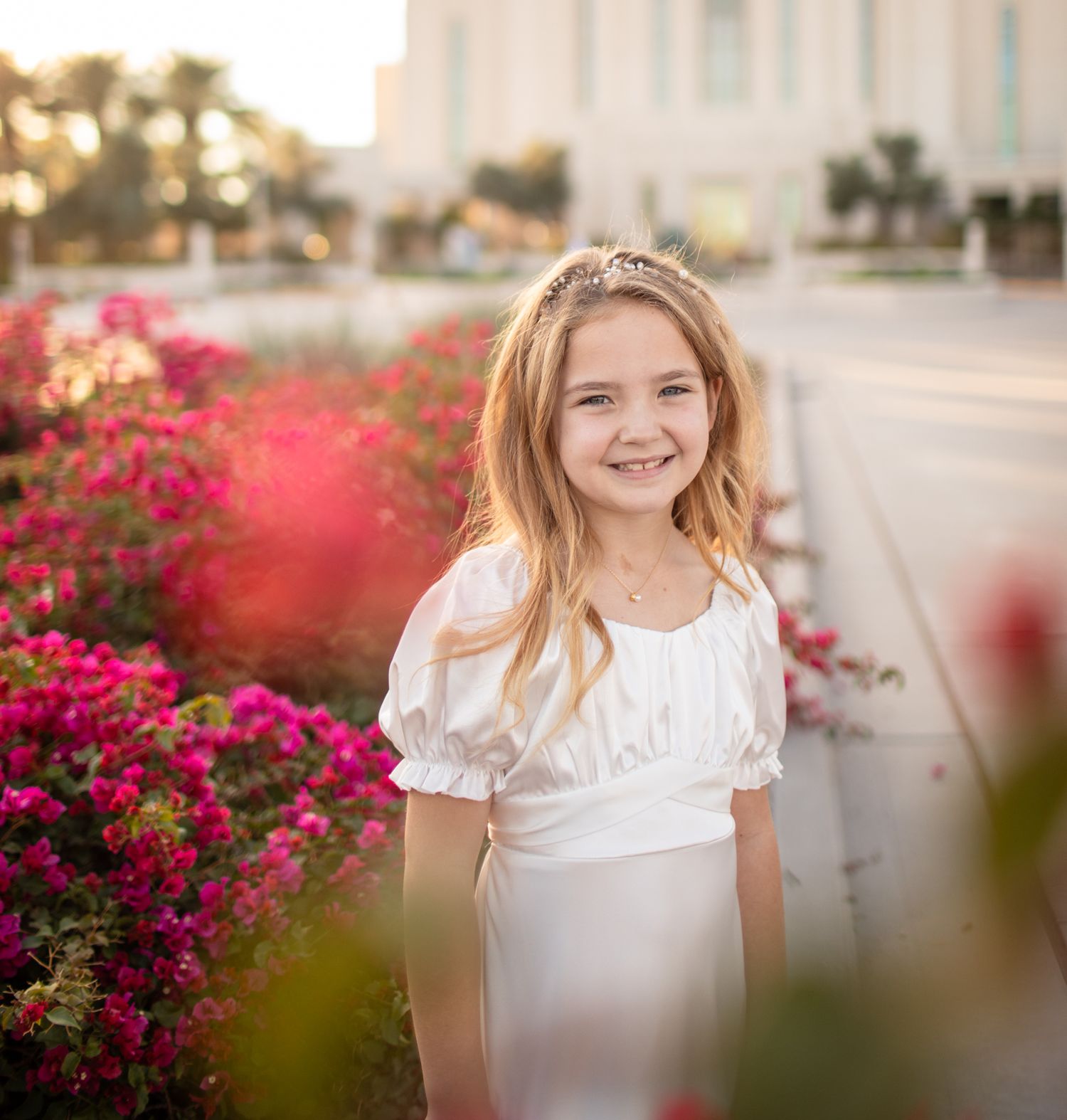 Young girl in white dress standing among vibrant pink bougainvillea flowers in front of the Gilbert, Arizona temple.